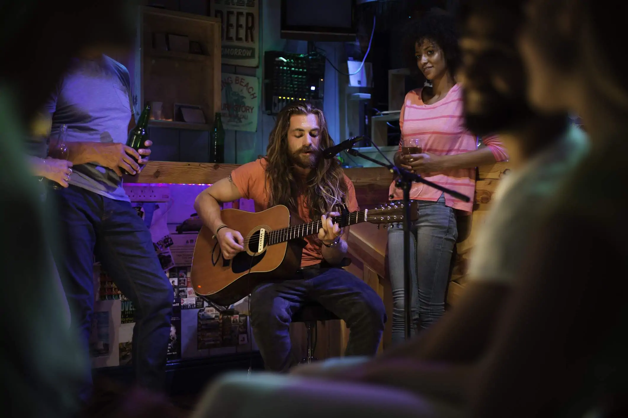 Image depicts a person holding a guitar and singing into a microphone as people gather around.