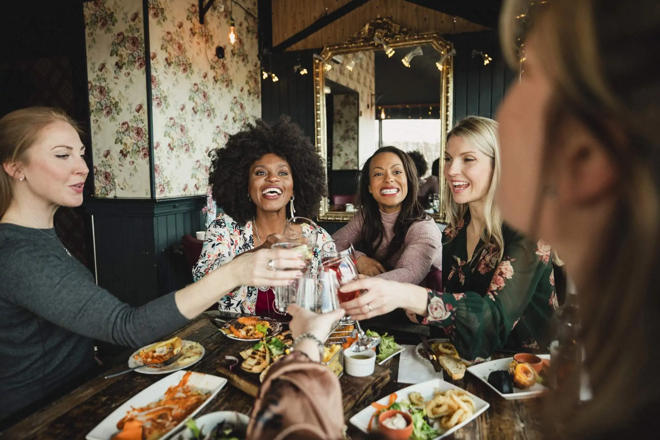 Image depicts a group of people cheersing glasses at a table in a restaurant.