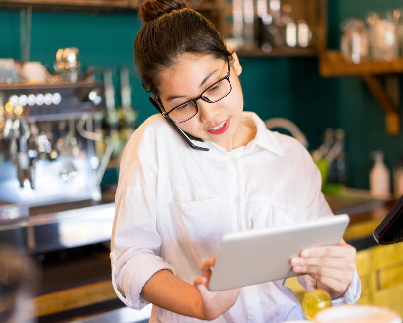 Image depicts a restaurant worker using a tablet to take a reservation over the phone.