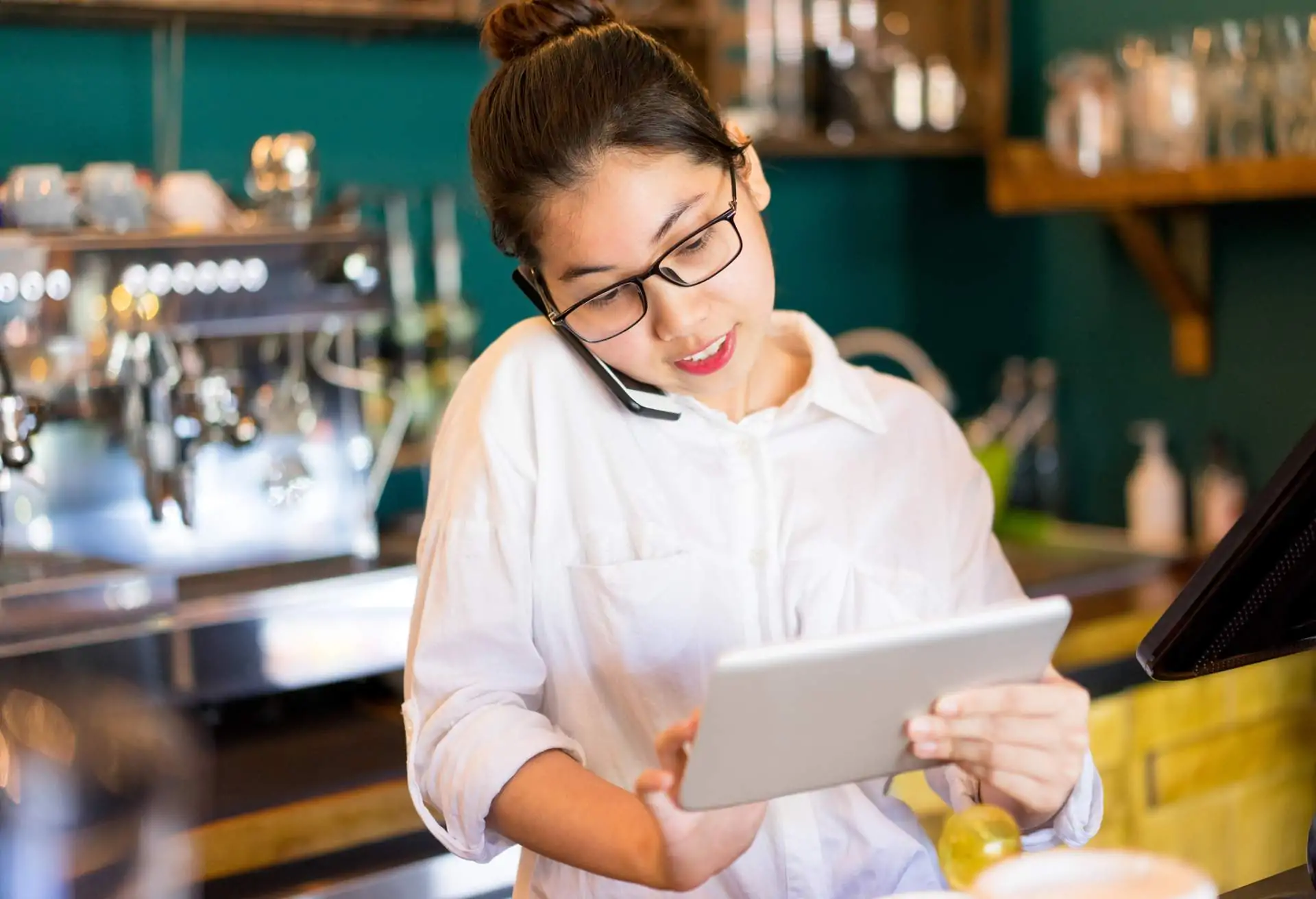 Image depicts a restaurant worker using a tablet to take a reservation over the phone.