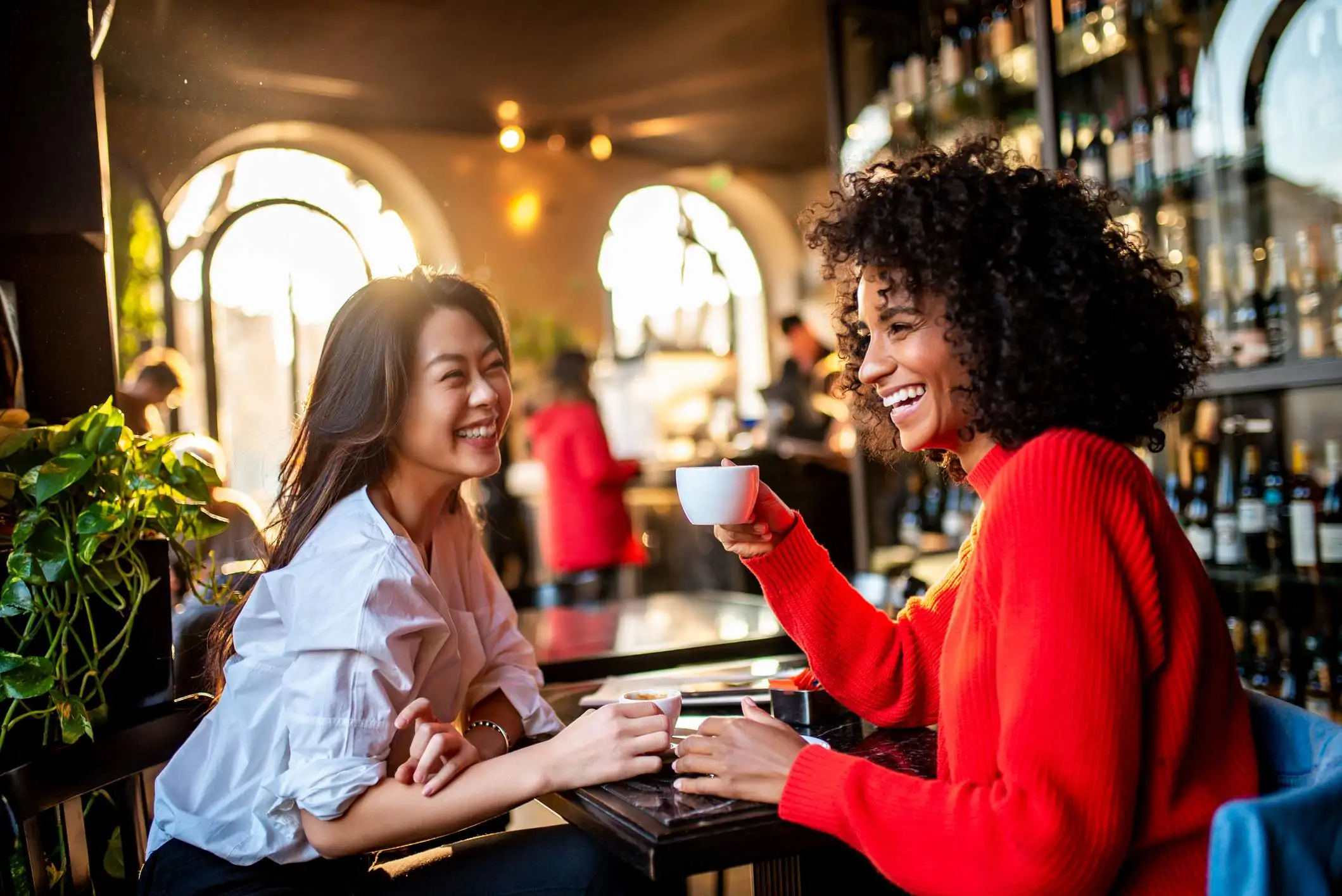 Image depicts two guests having coffee together. One is wearing a white button down shirt and the other is wearing a festive red sweater.