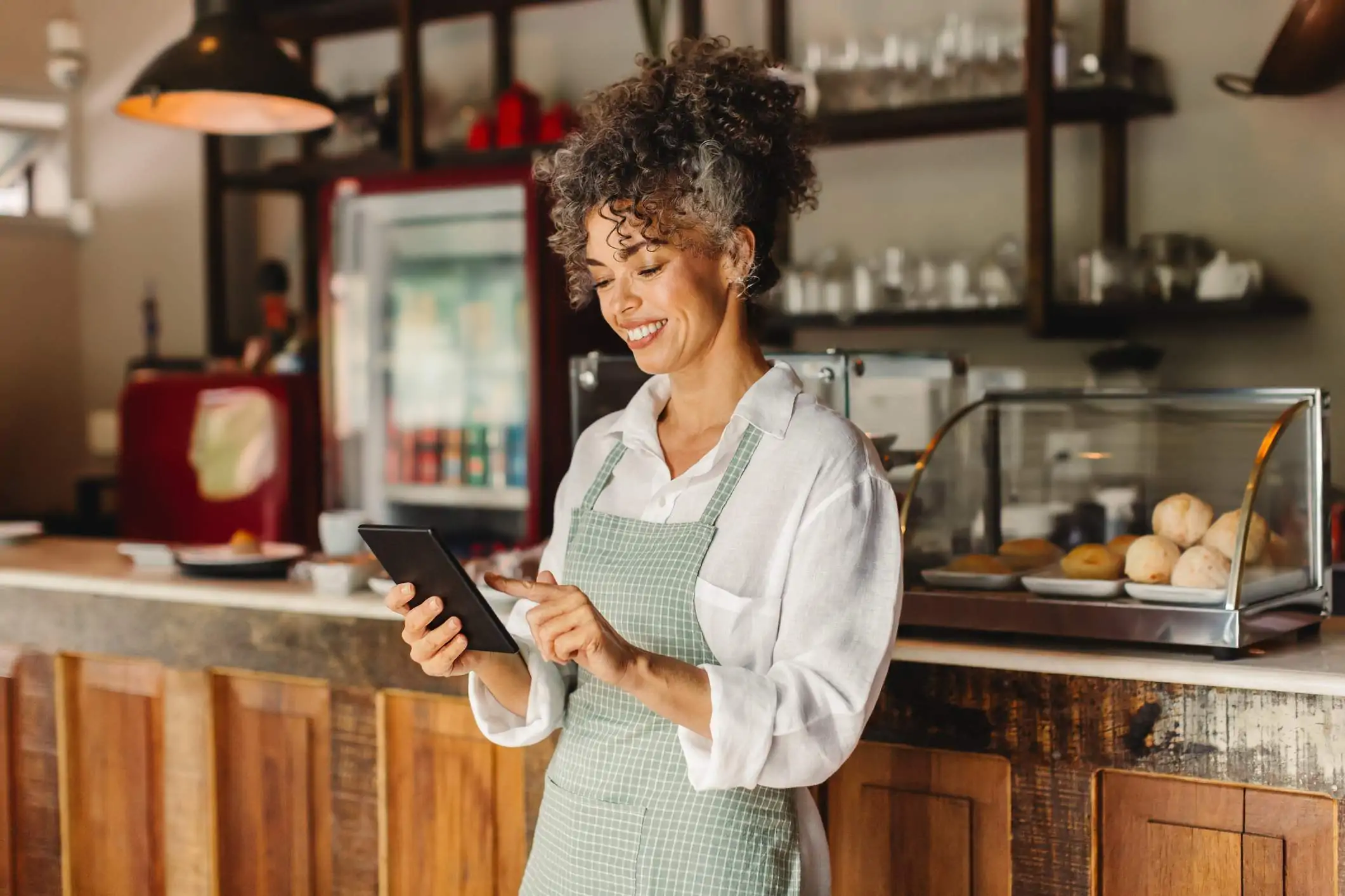 Image depicts a server wearing a green and white plaid apron using a tablet.