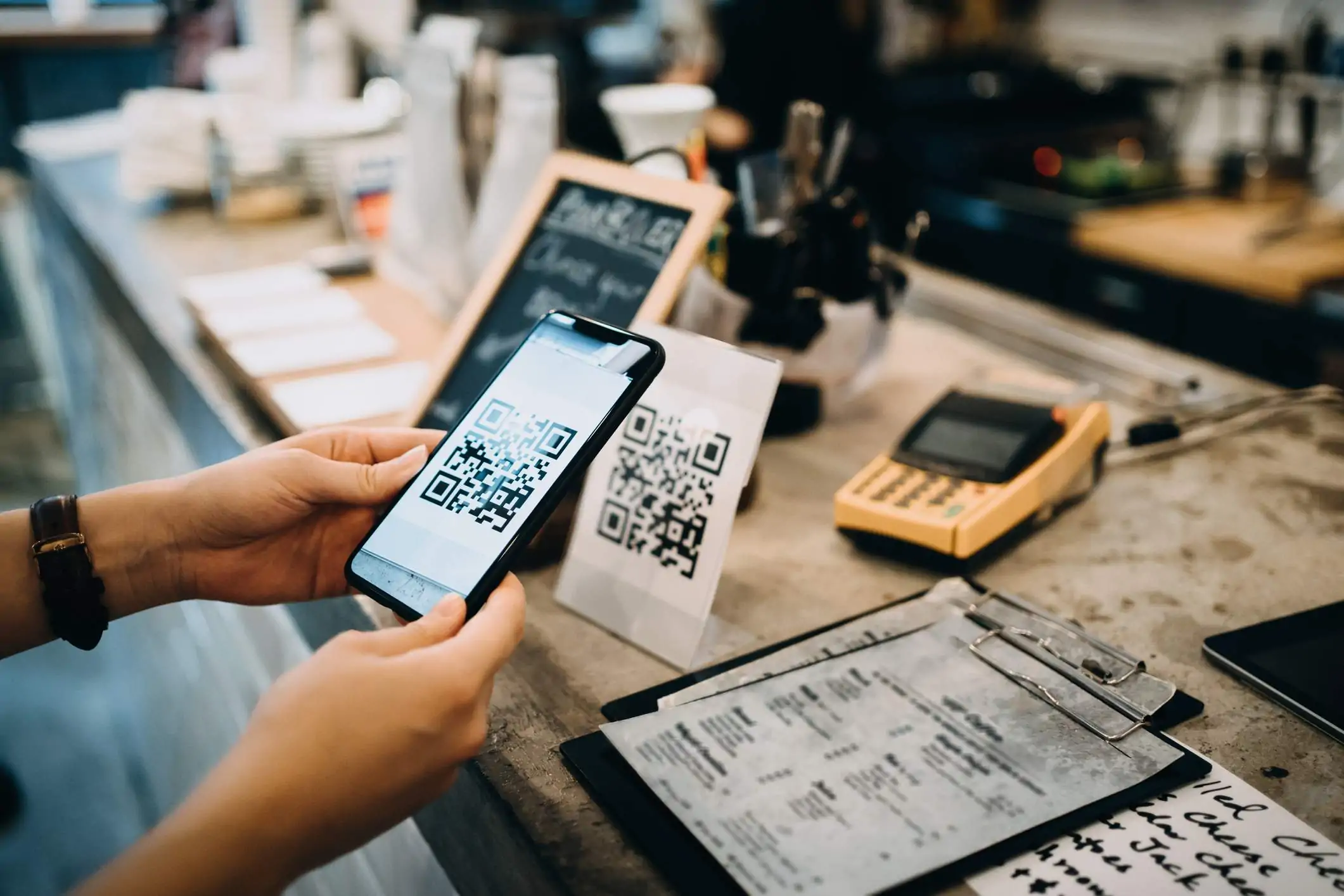 Image depicts a person holding a phone up to a restaurant counter and scanning a QR code.