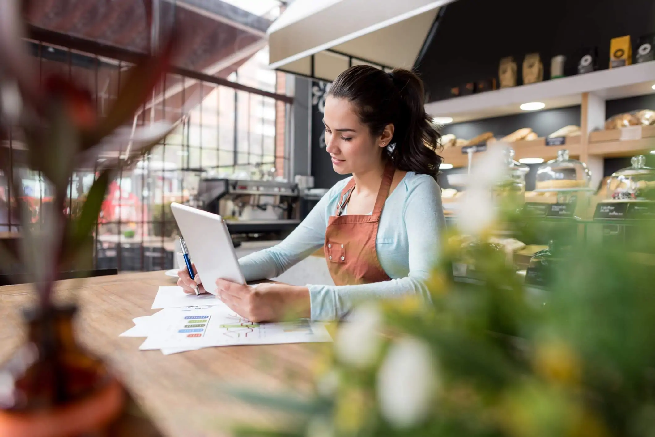 Image depicts a restaurant worker wearing a brown apron using a tablet.