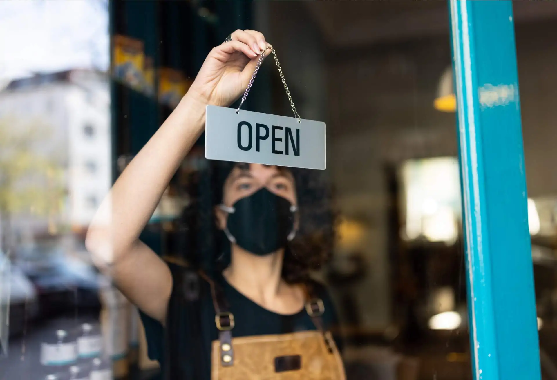 Restaurant employee in black apron behind a glass door flips a sign to read “open”