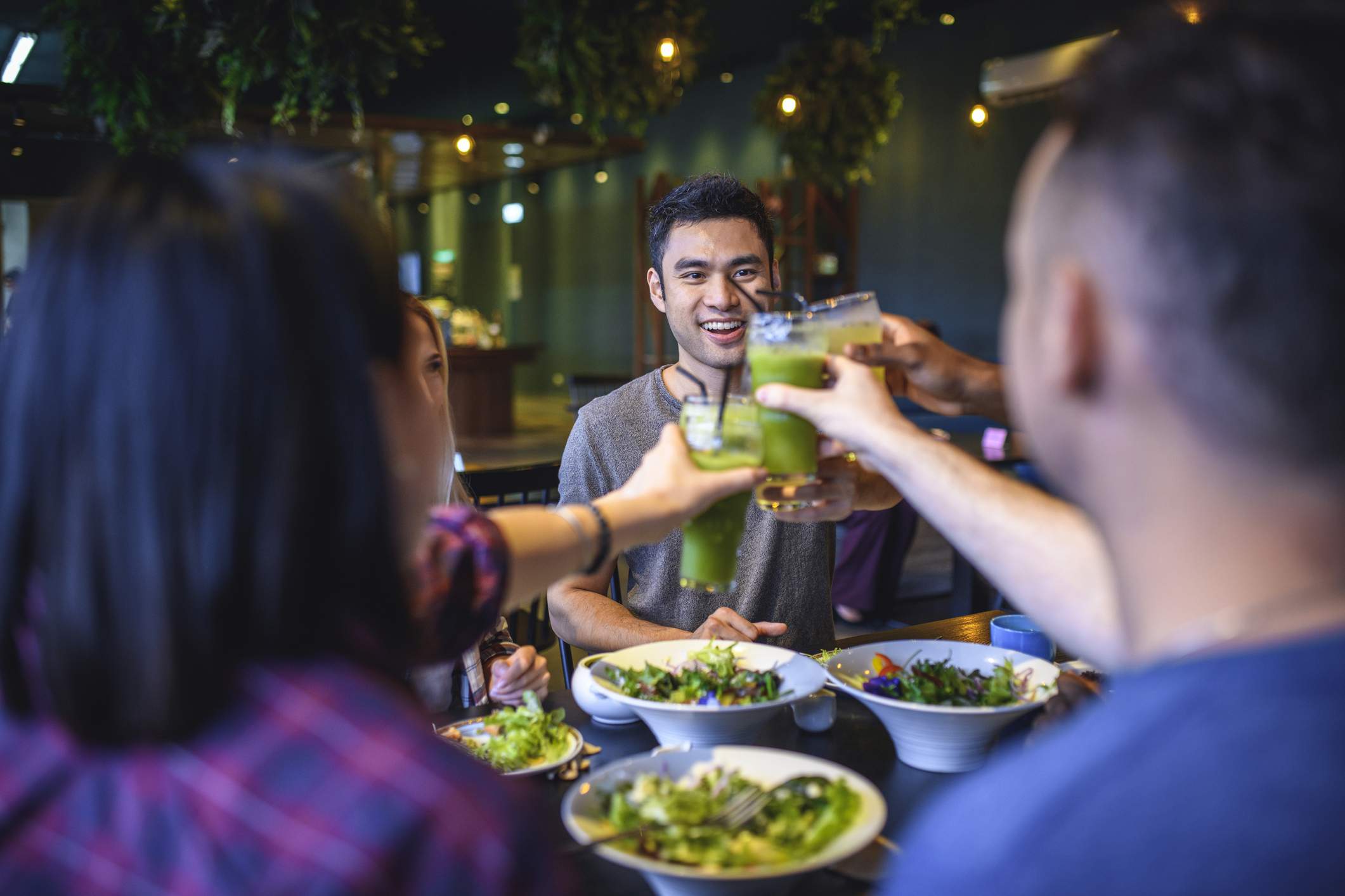 Image depicts a group of people cheersing green juices at a restaurant.