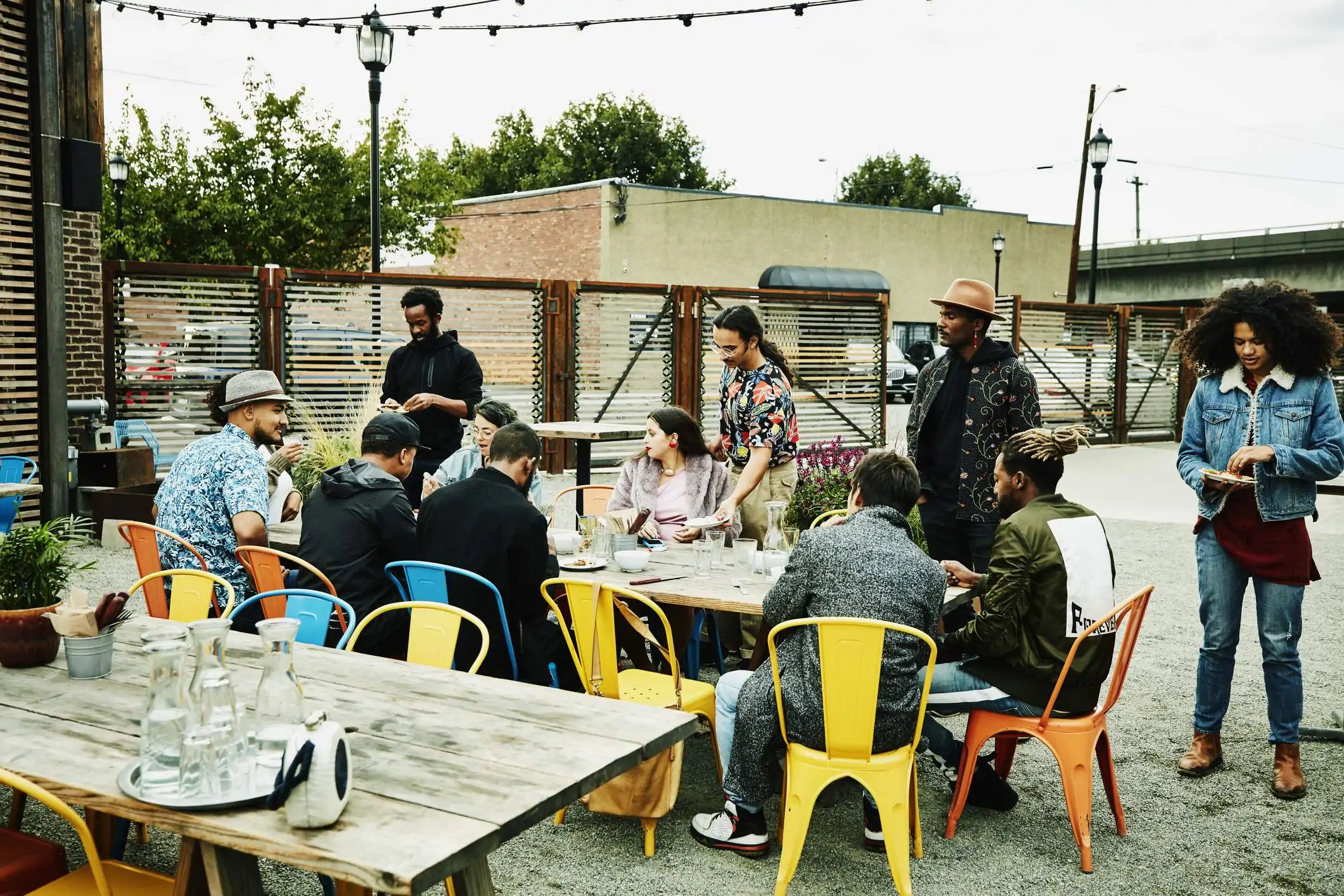 Image depicts a person sitting outside cheersing a beer to another restaurant guest.