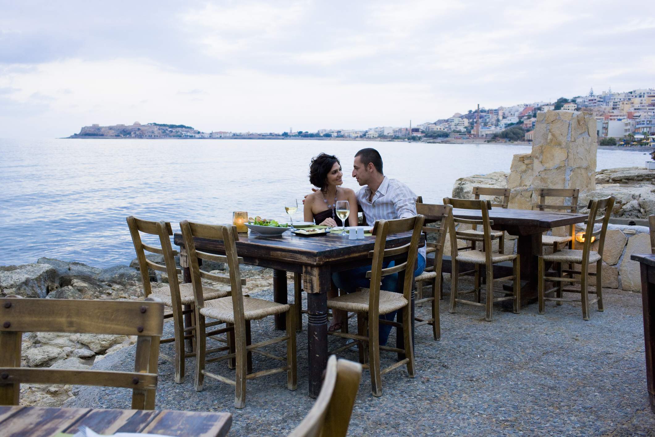 Image depicts a couple sitting at a restaurant table outside near the water.