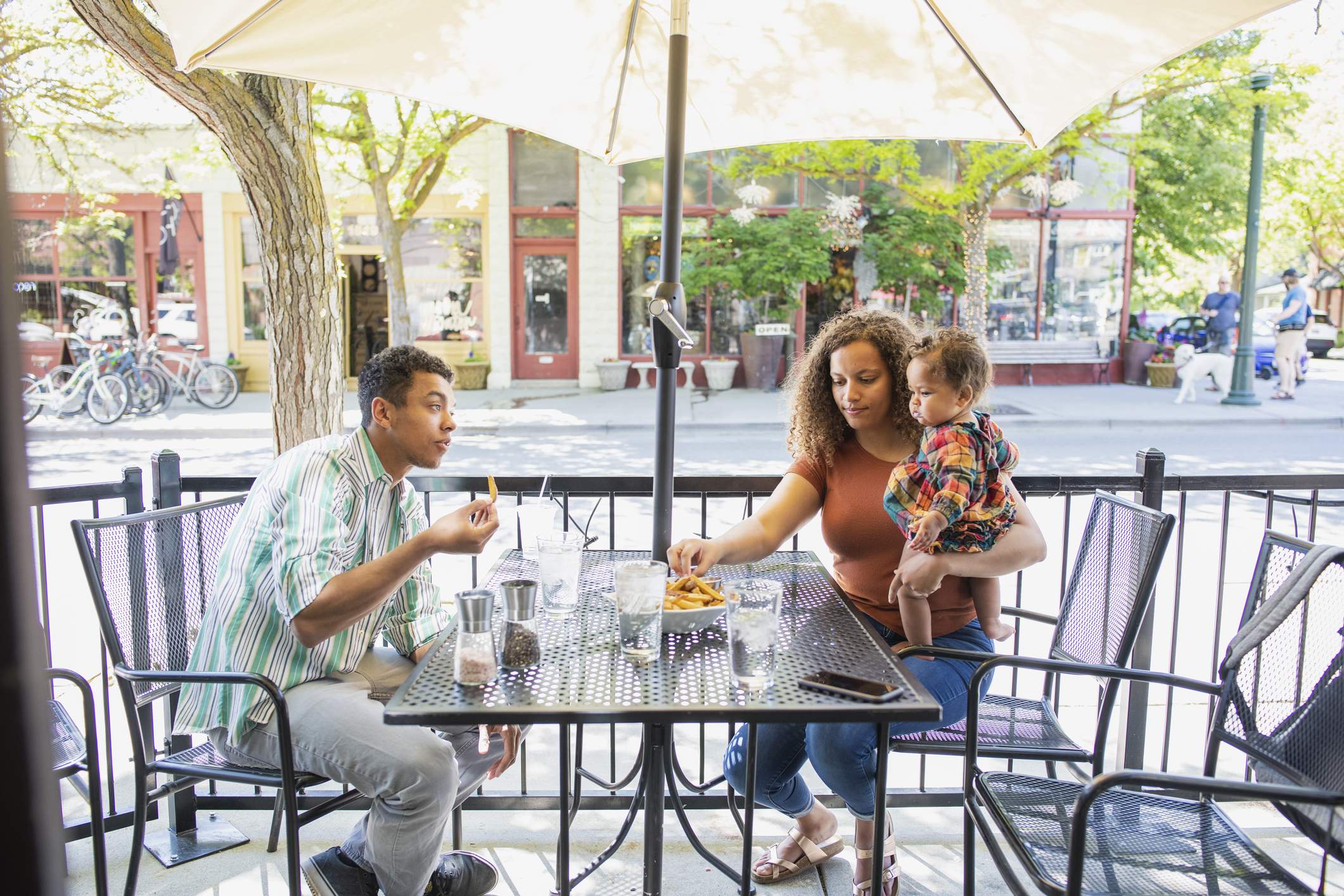 Image depicts a family sitting at an outdoor table eating french fries.