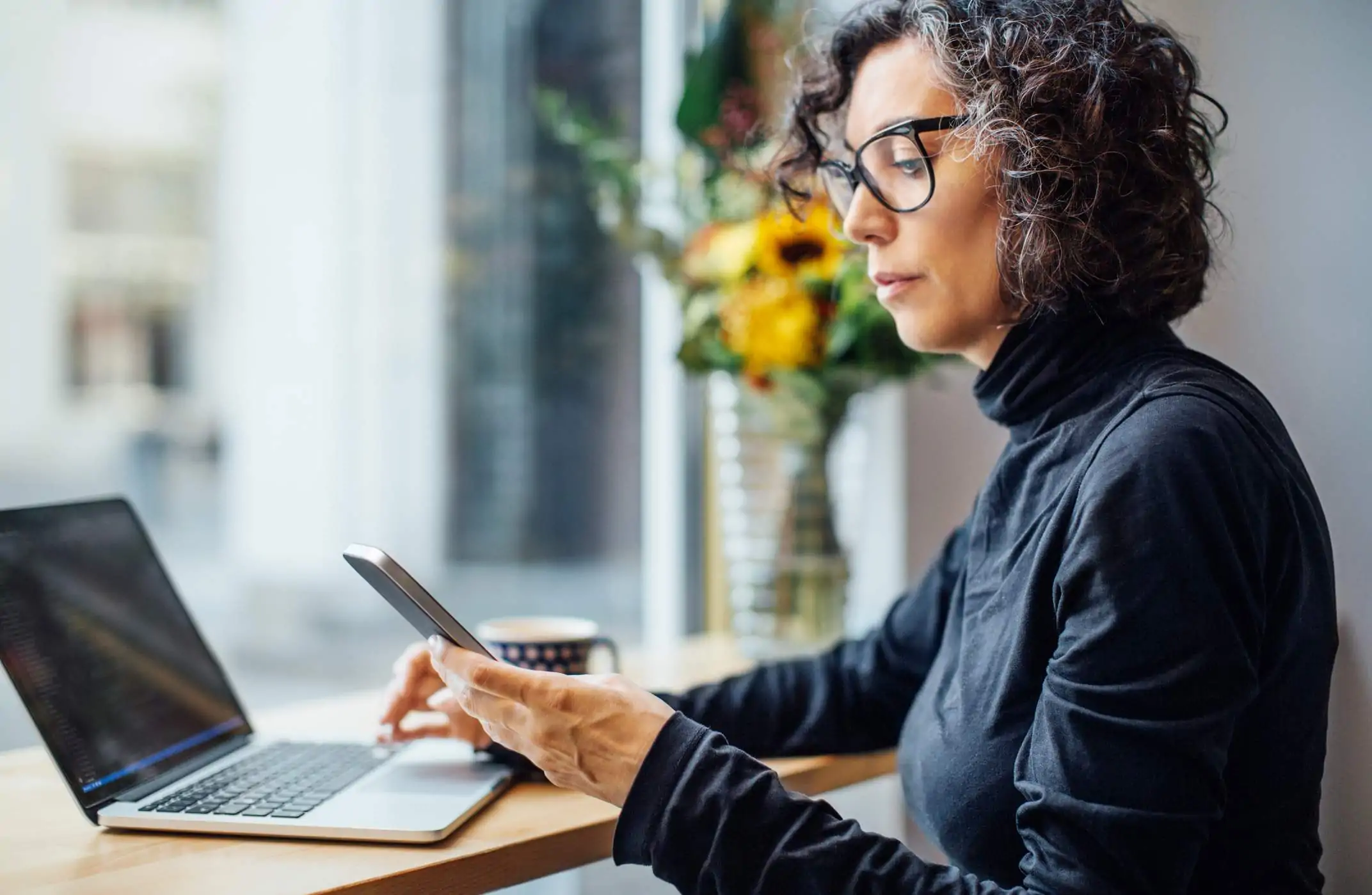 Image depicts a restaurant worker looking at a phone while working on a computer.