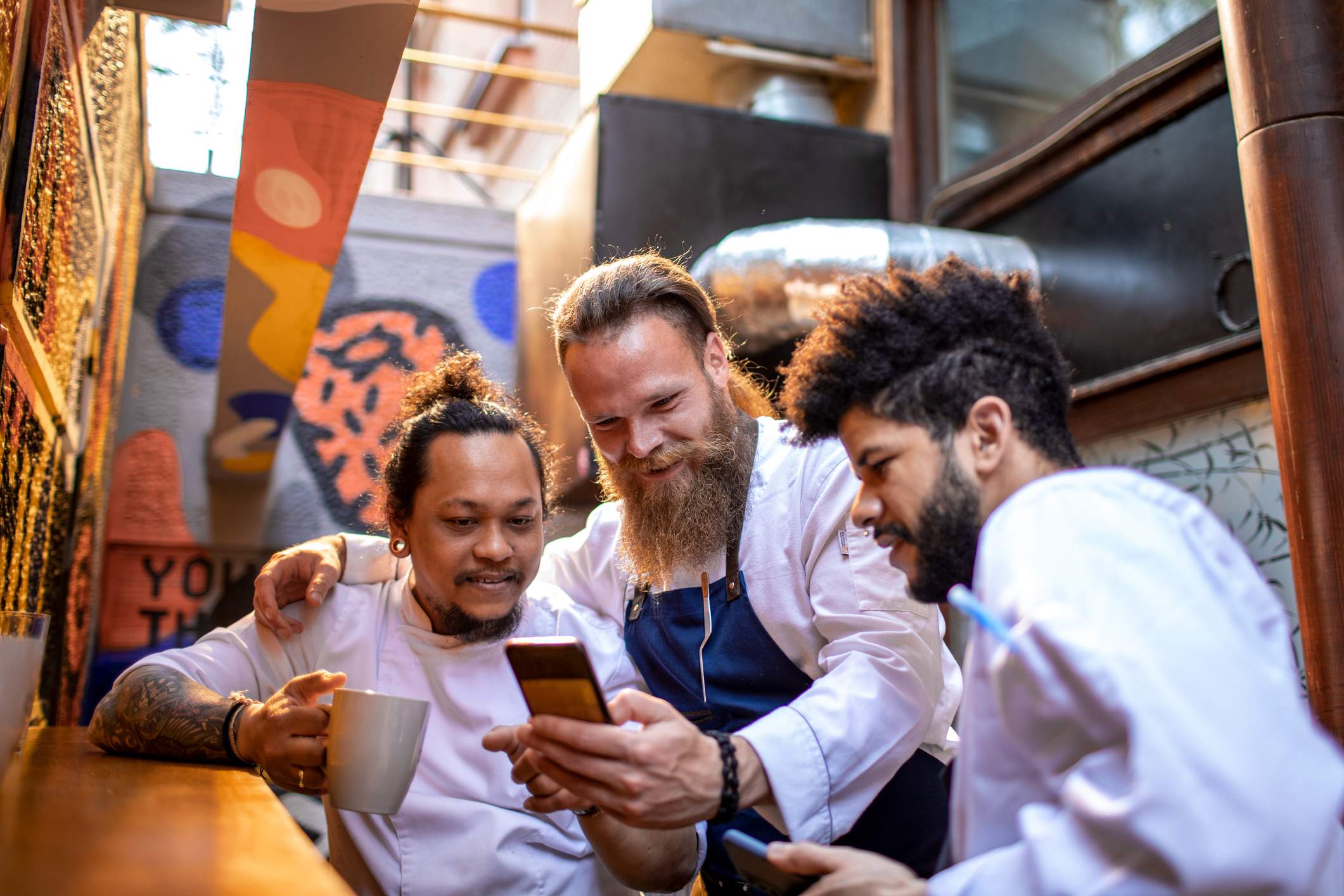 Image depicts three restaurant workers looking at a phone. 