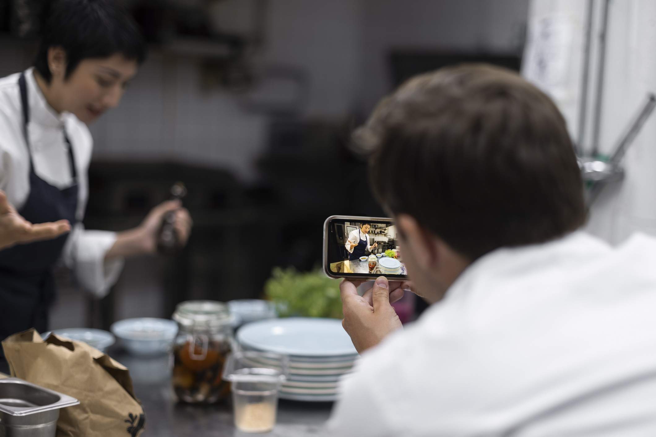 Image depicts a restaurant worker taking a video of another employee for social media. 