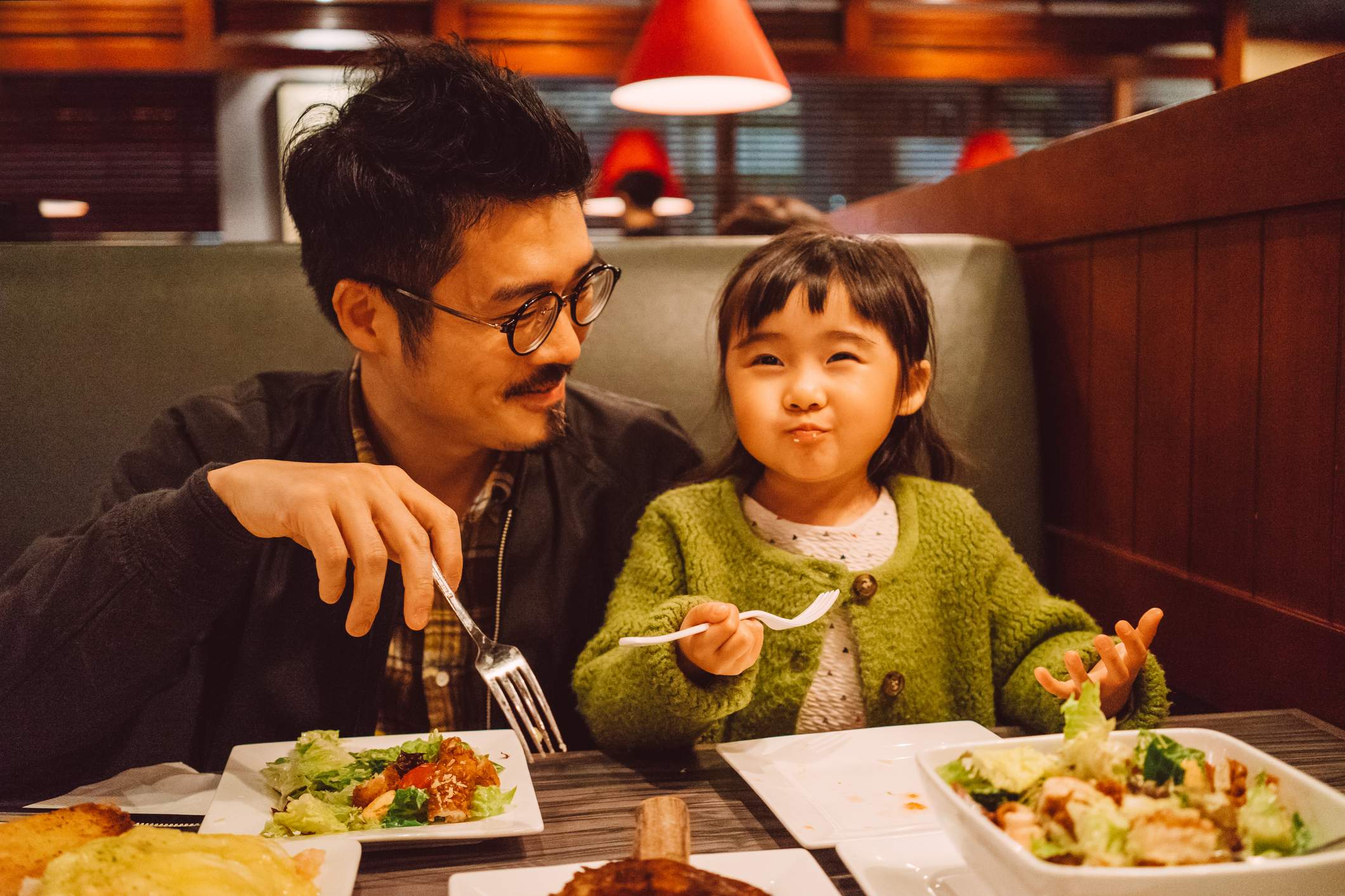 Image depicts a person and a child eating salads at a restaurant.