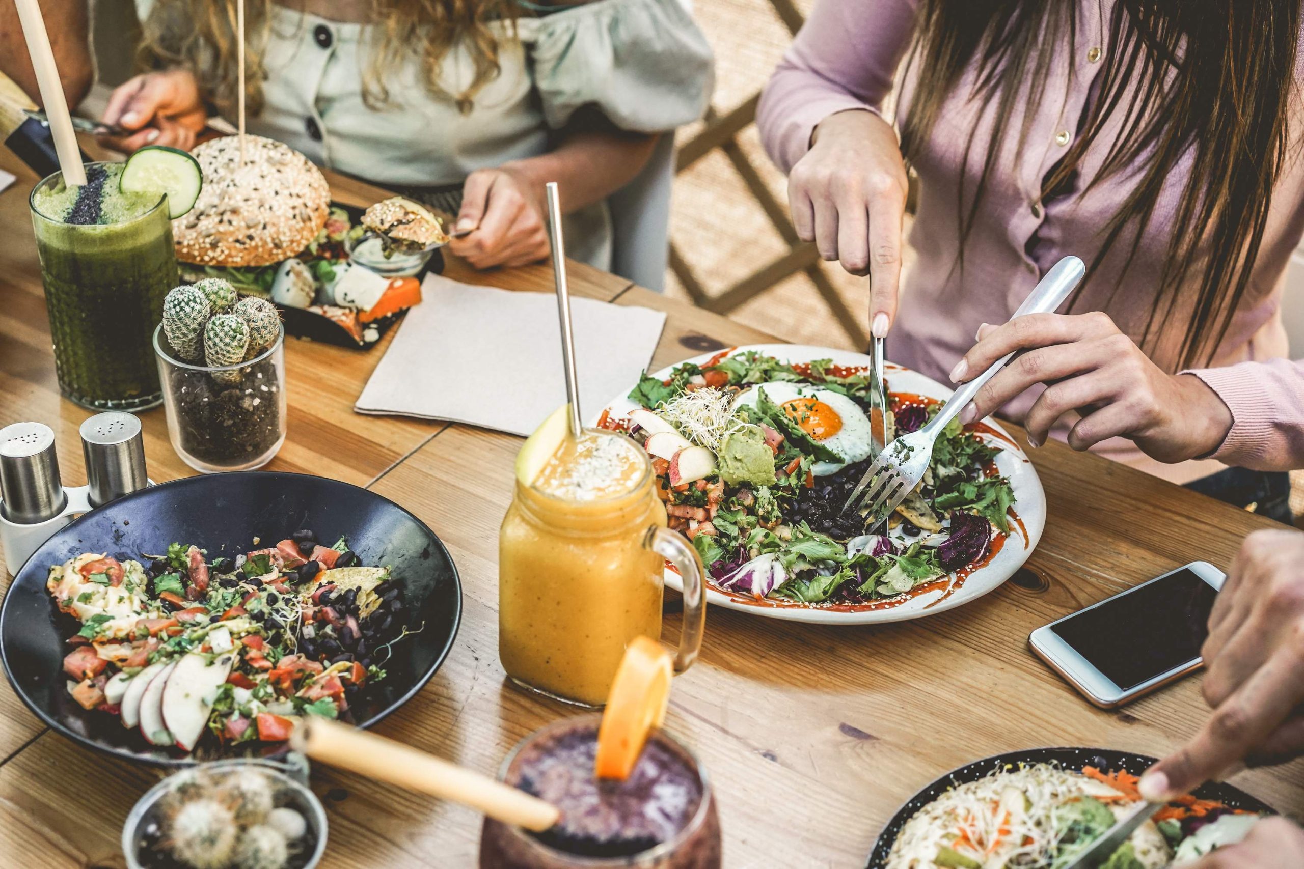 Image depicts diners out of frame eating an array of healthy foods and drinks at a restaurant.