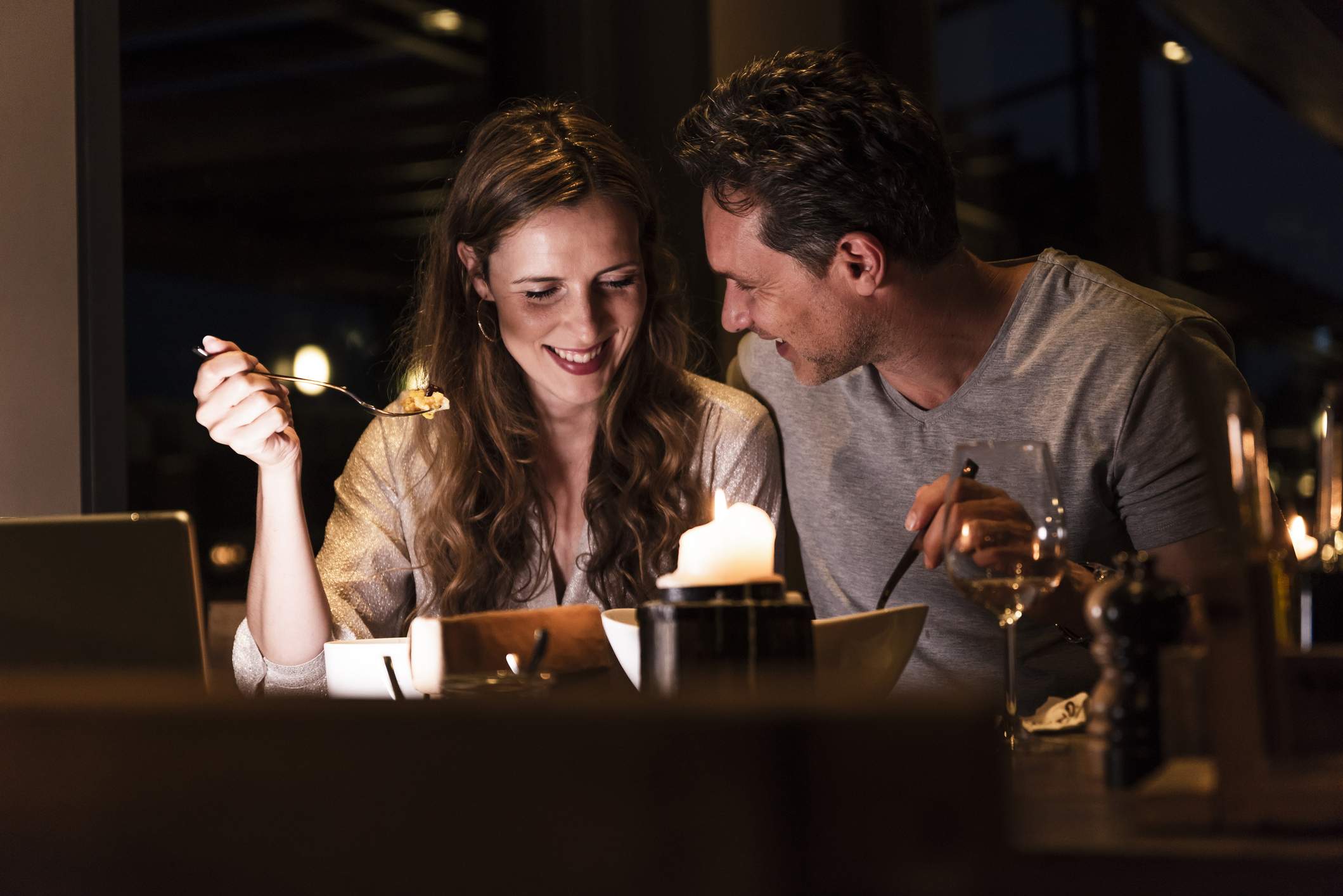 Image depicts two people sitting next to each other at a restaurant. They are sharing food and smiling. 