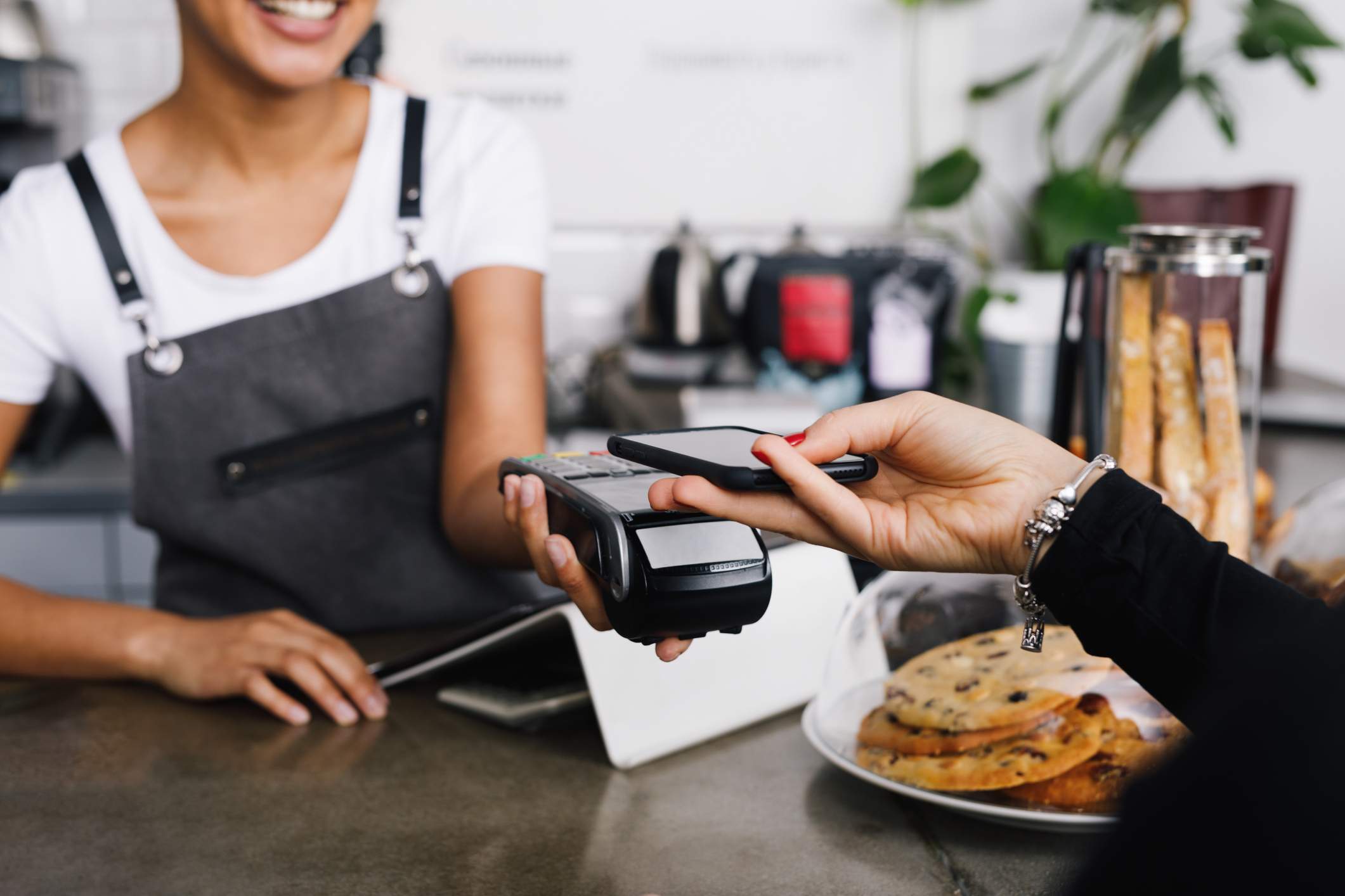 Image depicts a restaurant guest out of frame paying for a meal with a credit card. The server is holding out a point of sale system.