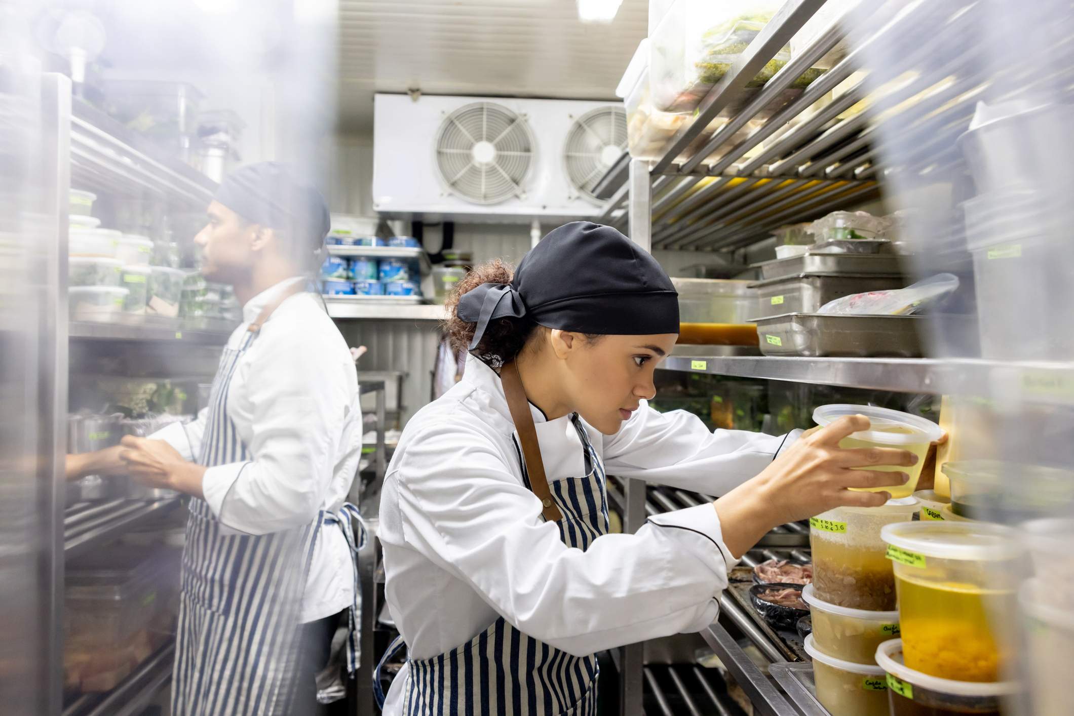 Image depicts two restaurant workers in a stock room. 