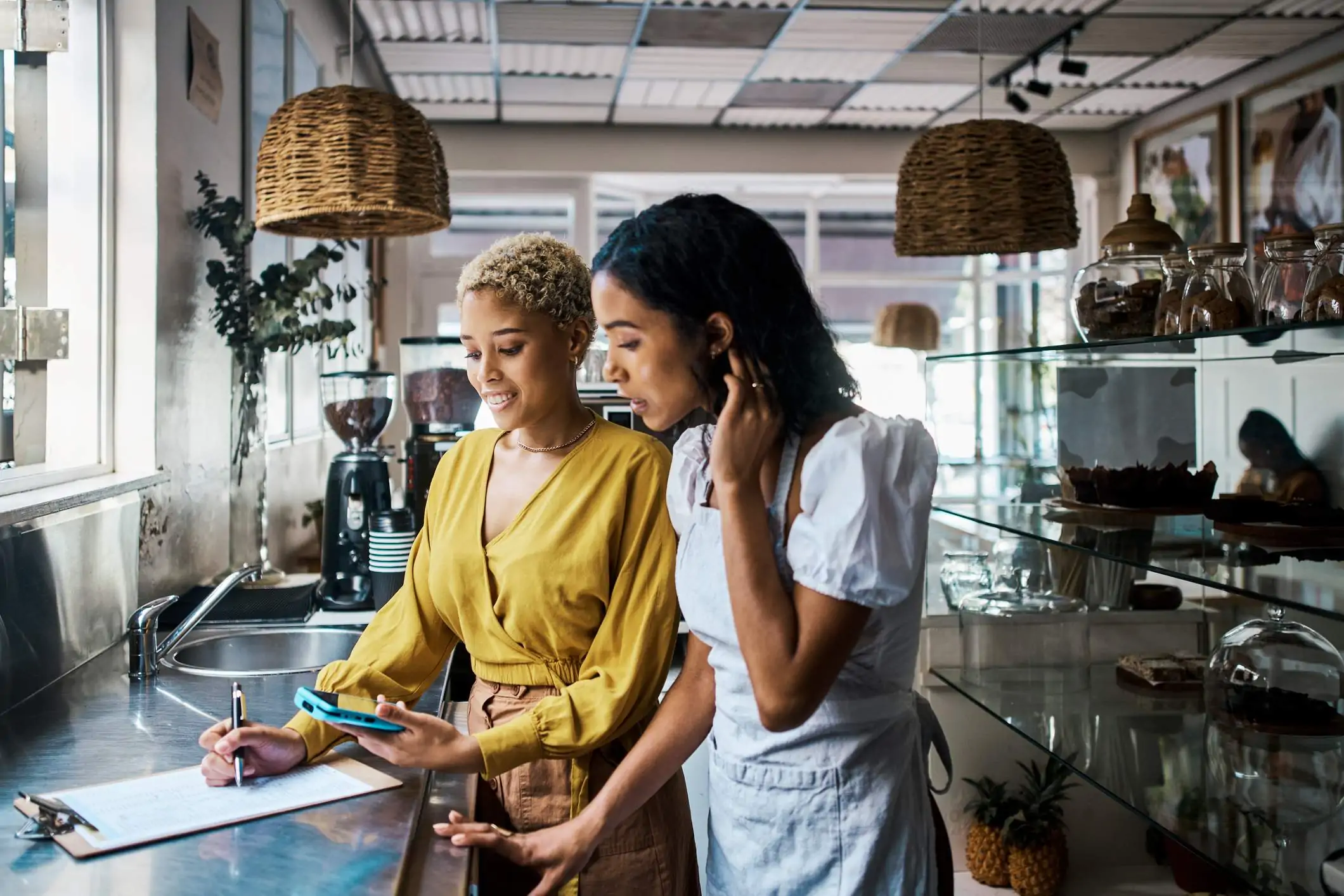 Image depicts two people looking at a phone and clipboard inside of a restaurant.