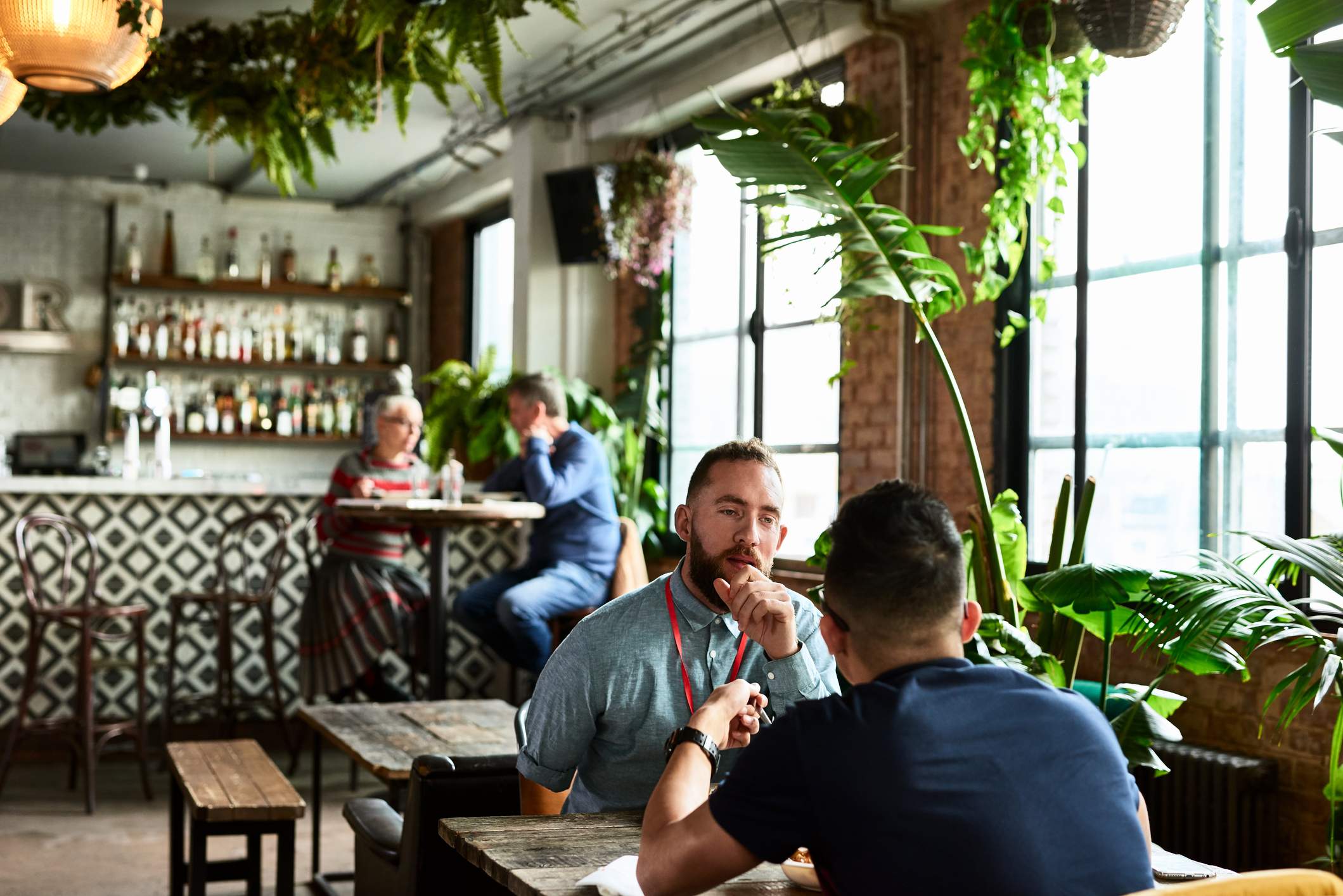 Image depicts two people speaking during an interview in a plant filled restaurant.