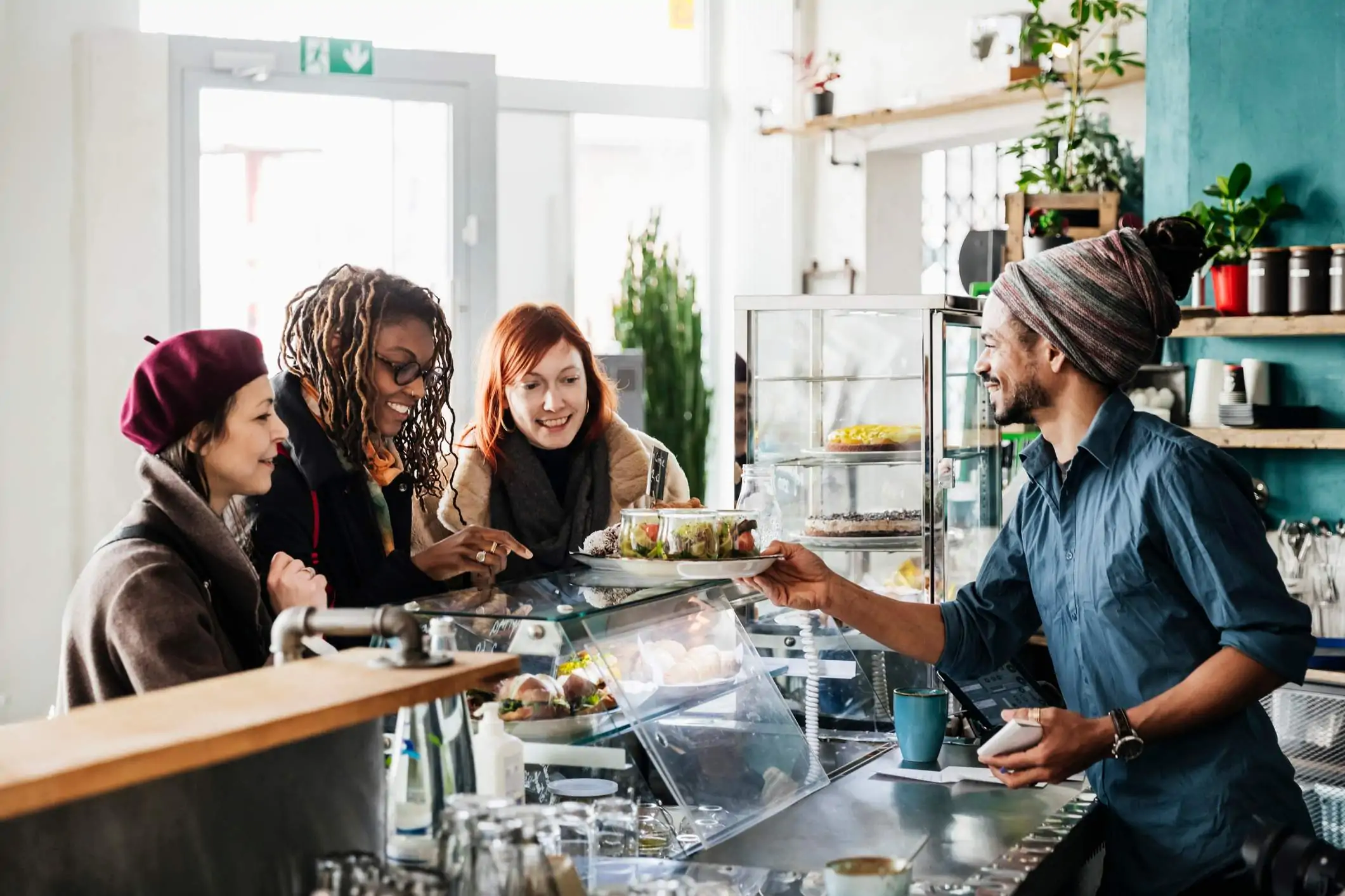 Image depicts a server behind a counter assisting three guests.