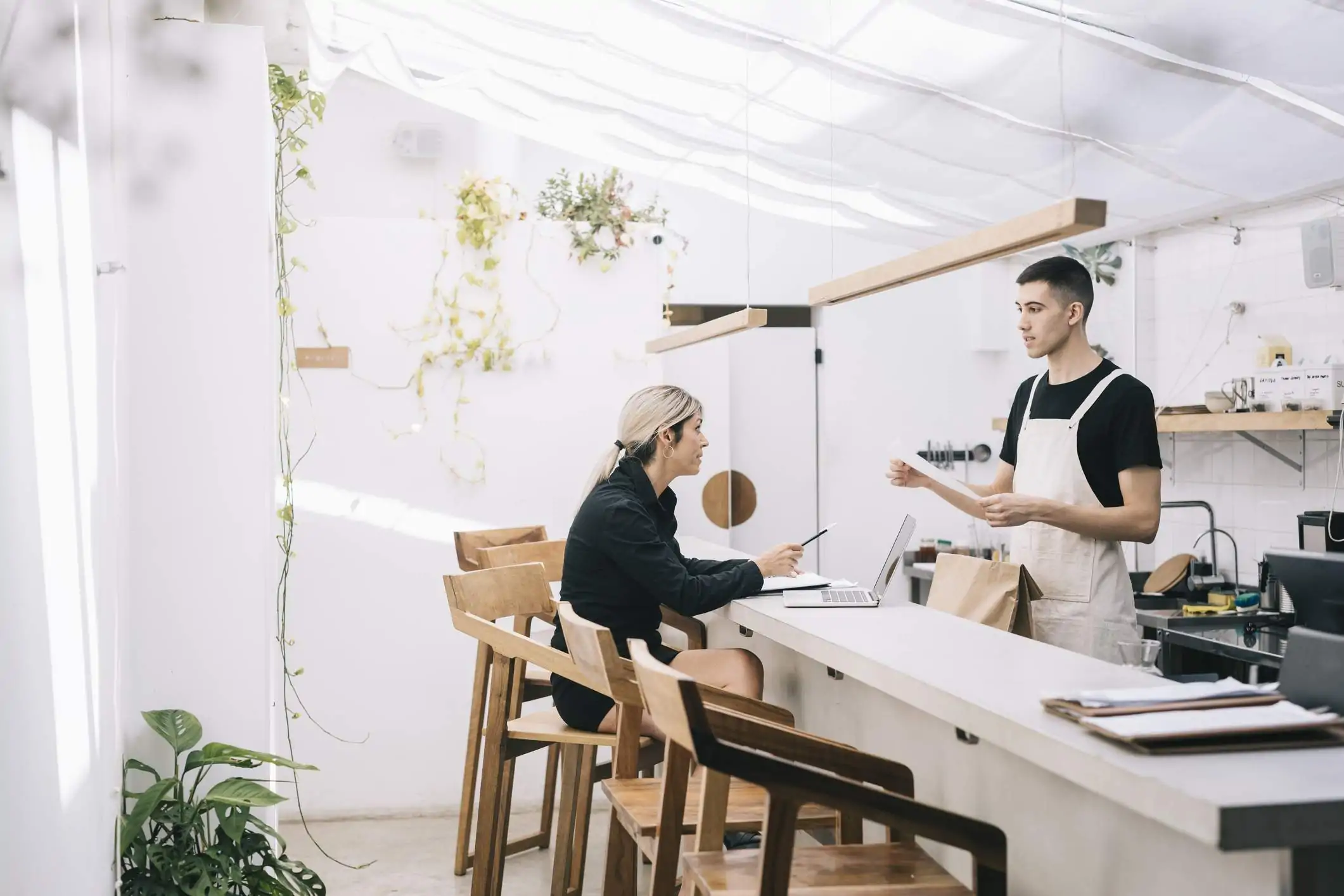 Image depicts two restaurant workers, one standing and one sitting, having a conversation.