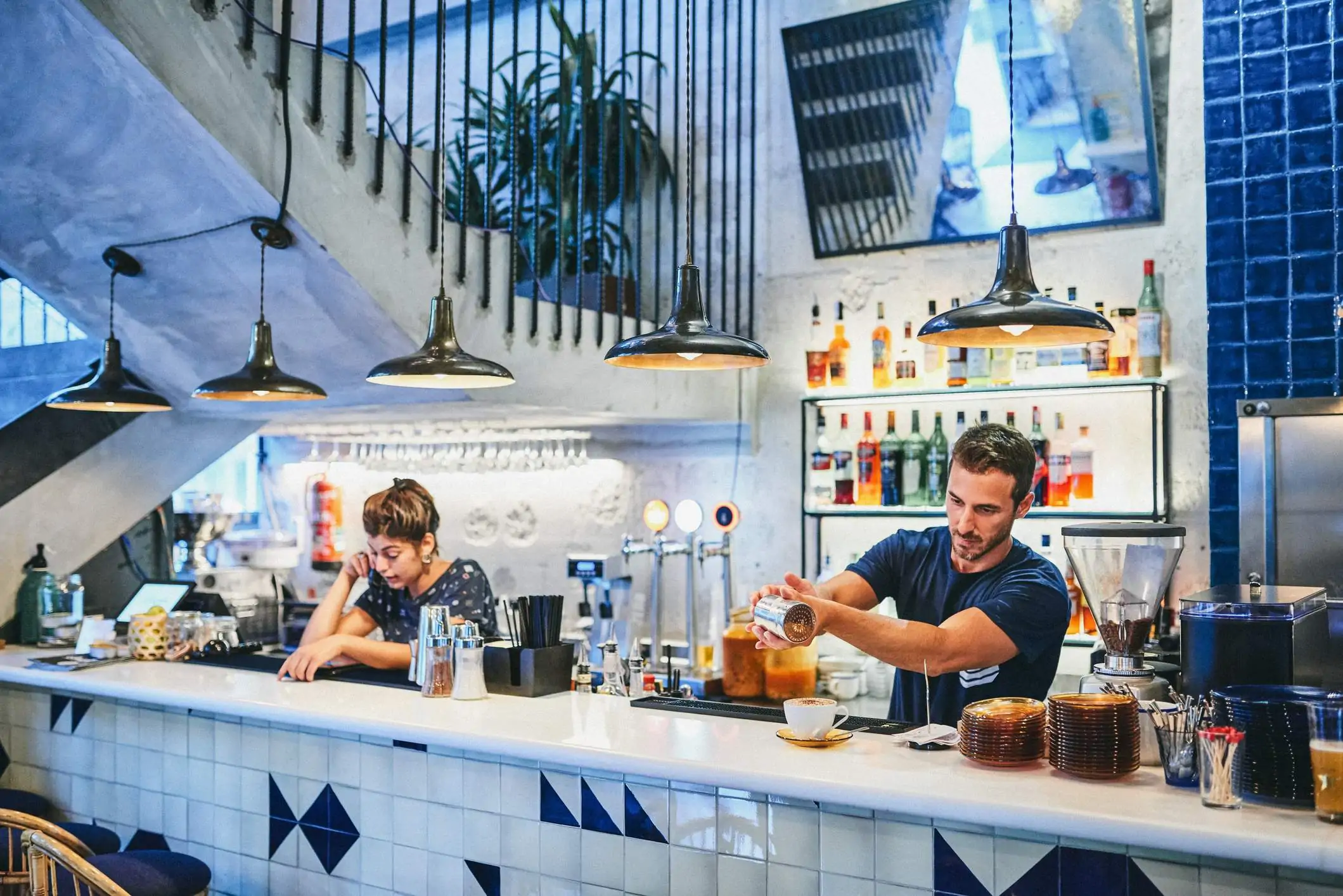 Image depicts two restaurant workers behind the bar, working separately.