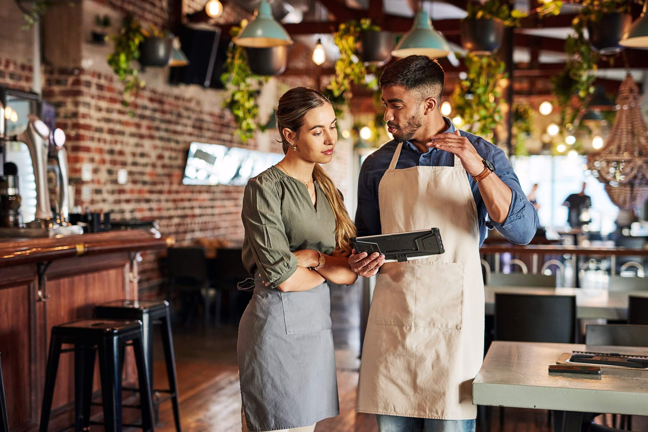 Image depicts two restaurant workers discussing something on a tablet.
