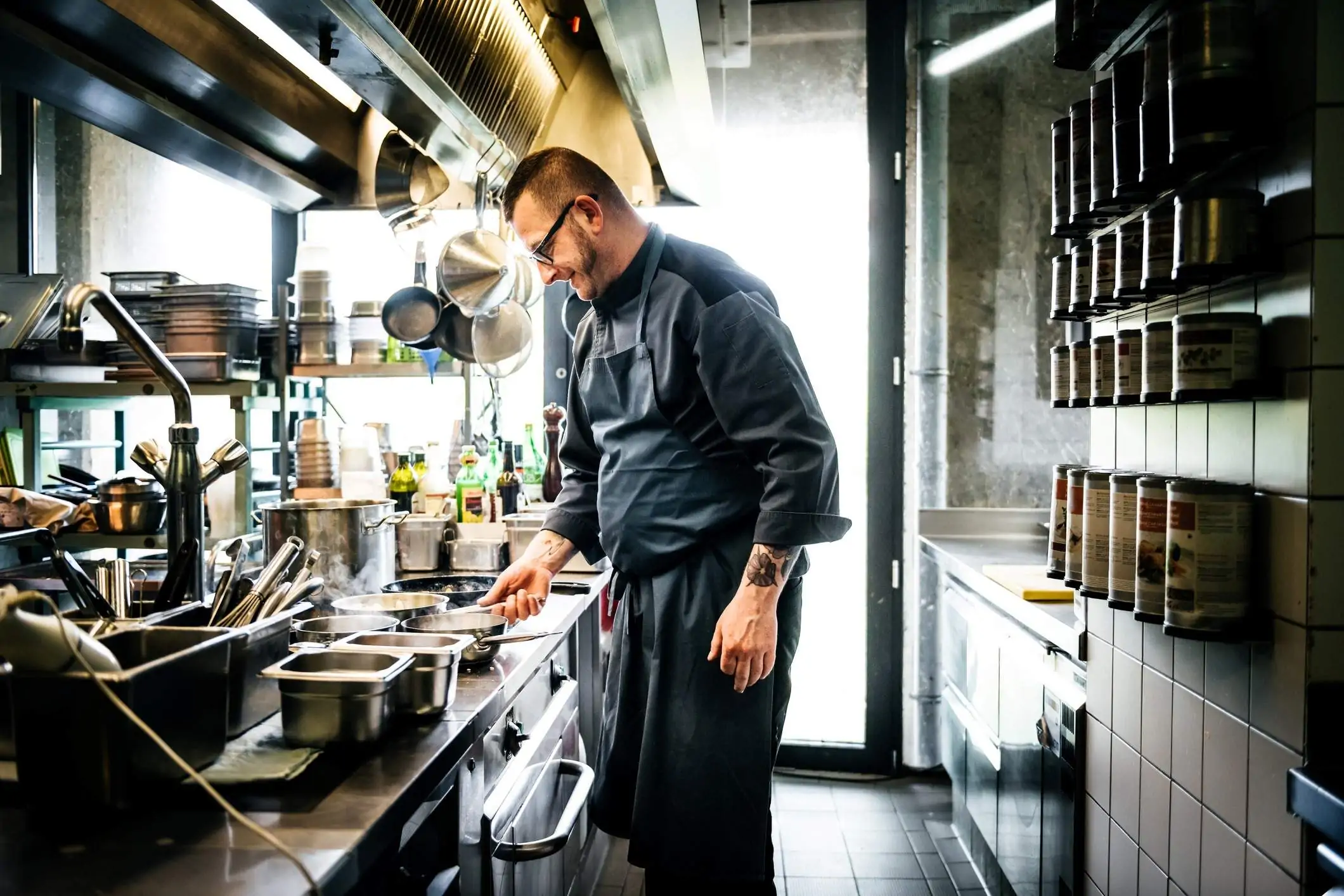 ​Image depicts a chef preparing food on a stove while wearing a navy apron.