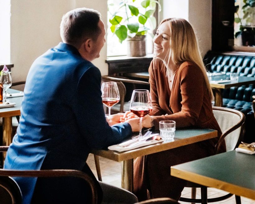 Image depicts two people having a conversation while sitting at a table in a restaurant.