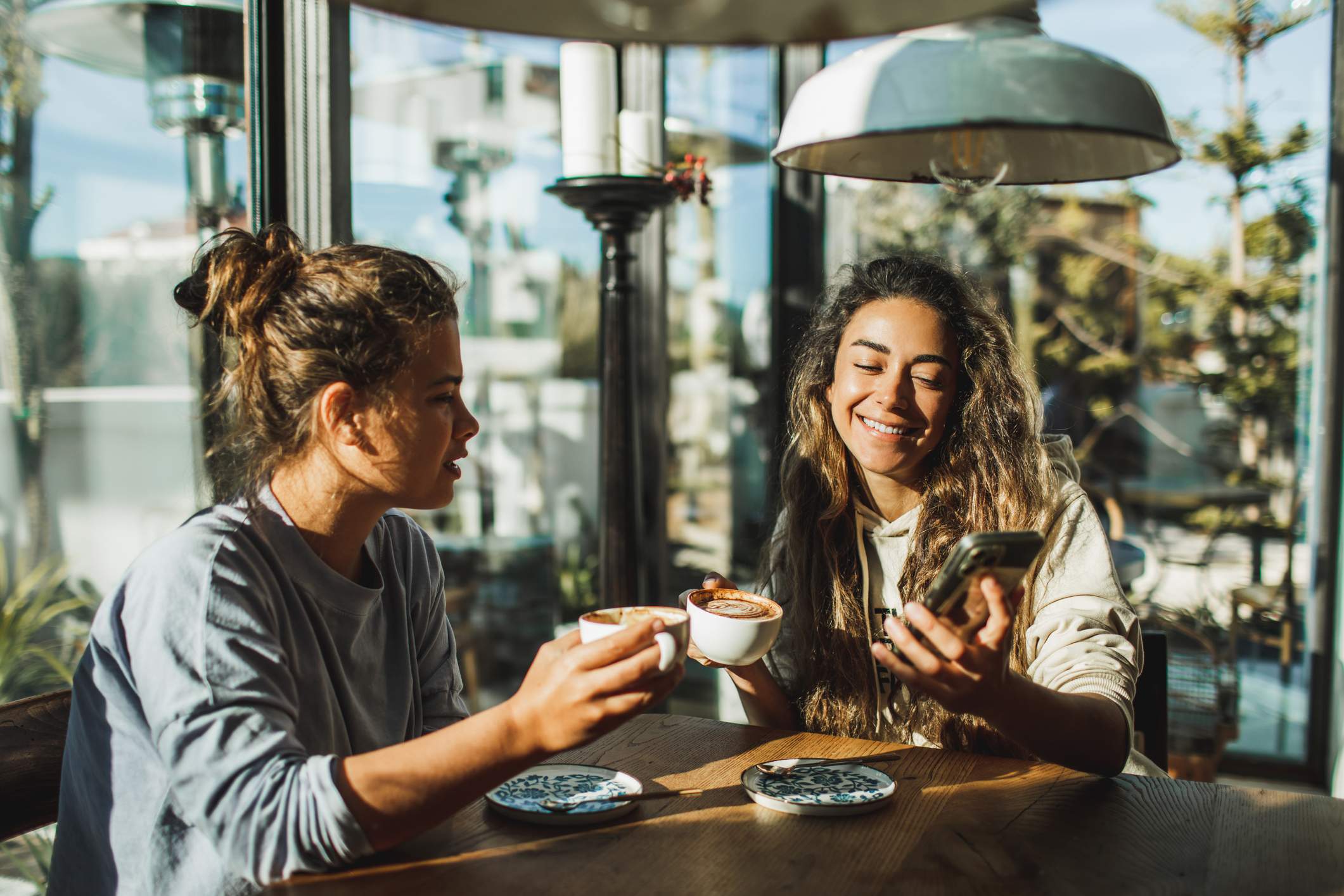 Image depicts two people drinking coffee and looking at a mobile phone in a restaurant. 
