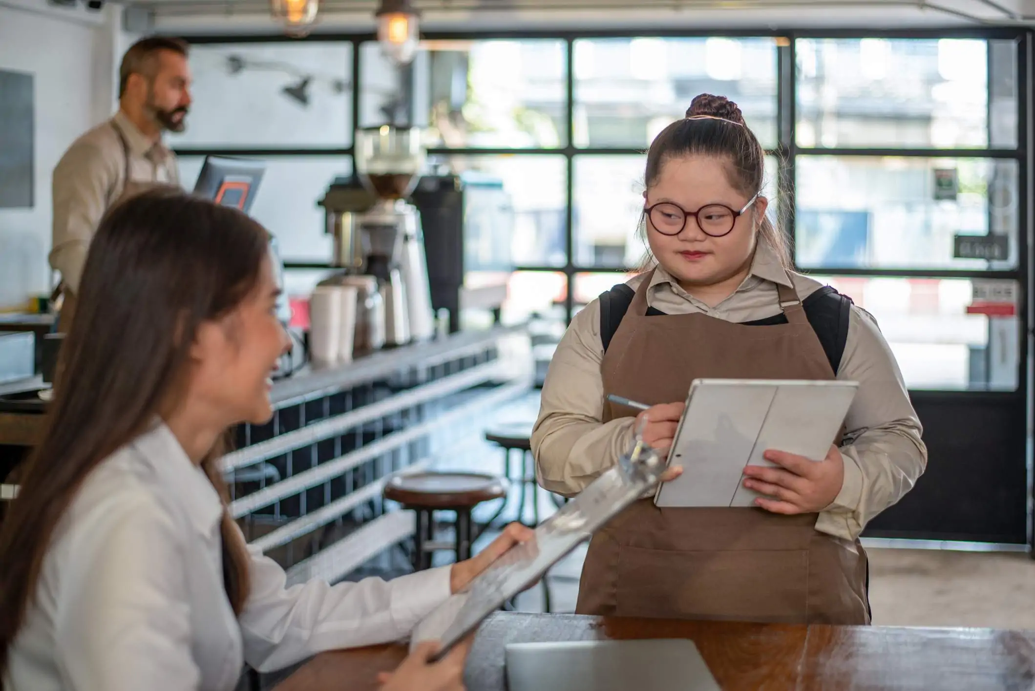 Image depicts a young server taking an order from a guest in a restaurant.