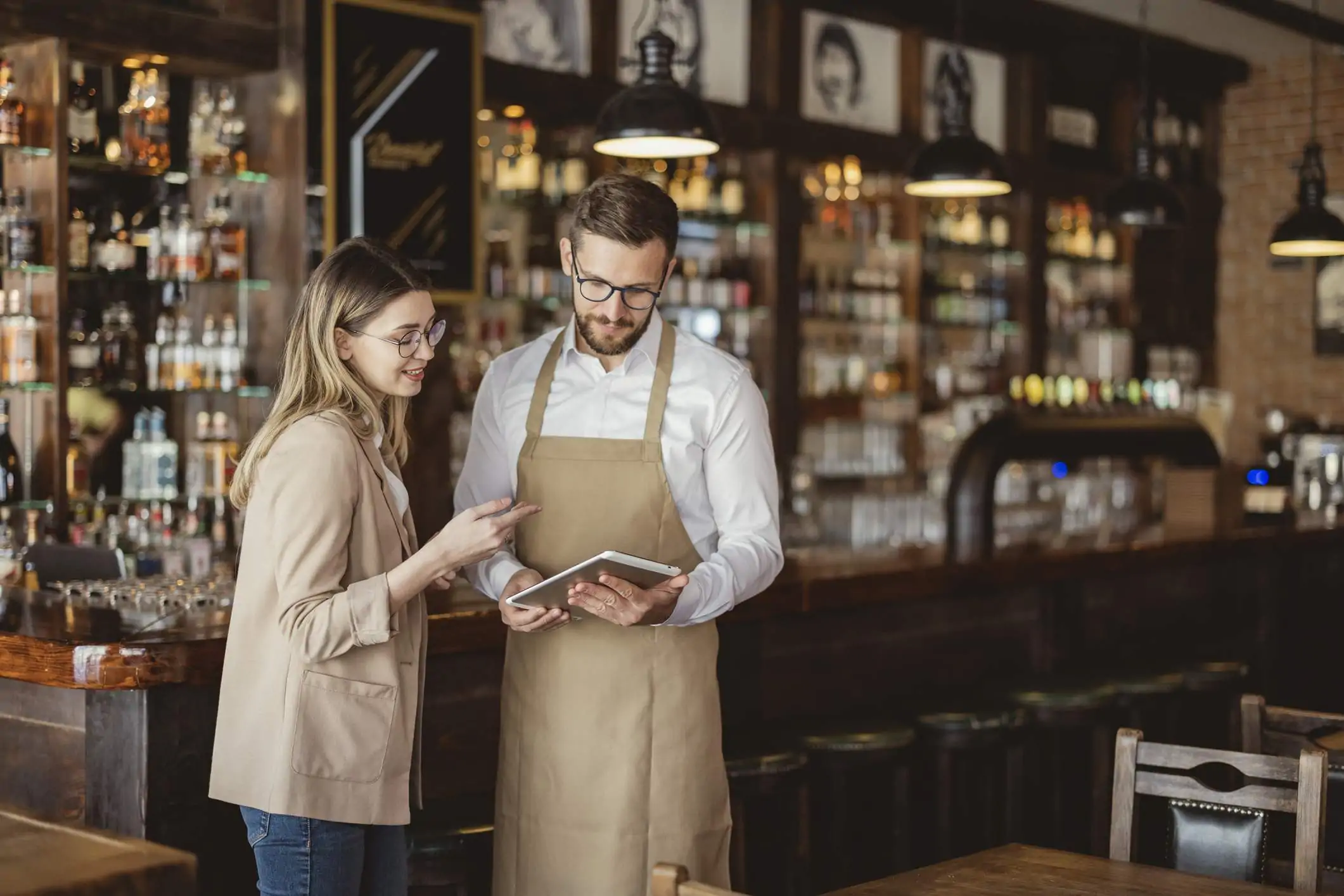 Image depicts two restaurant workers chatting as they look at a tablet.