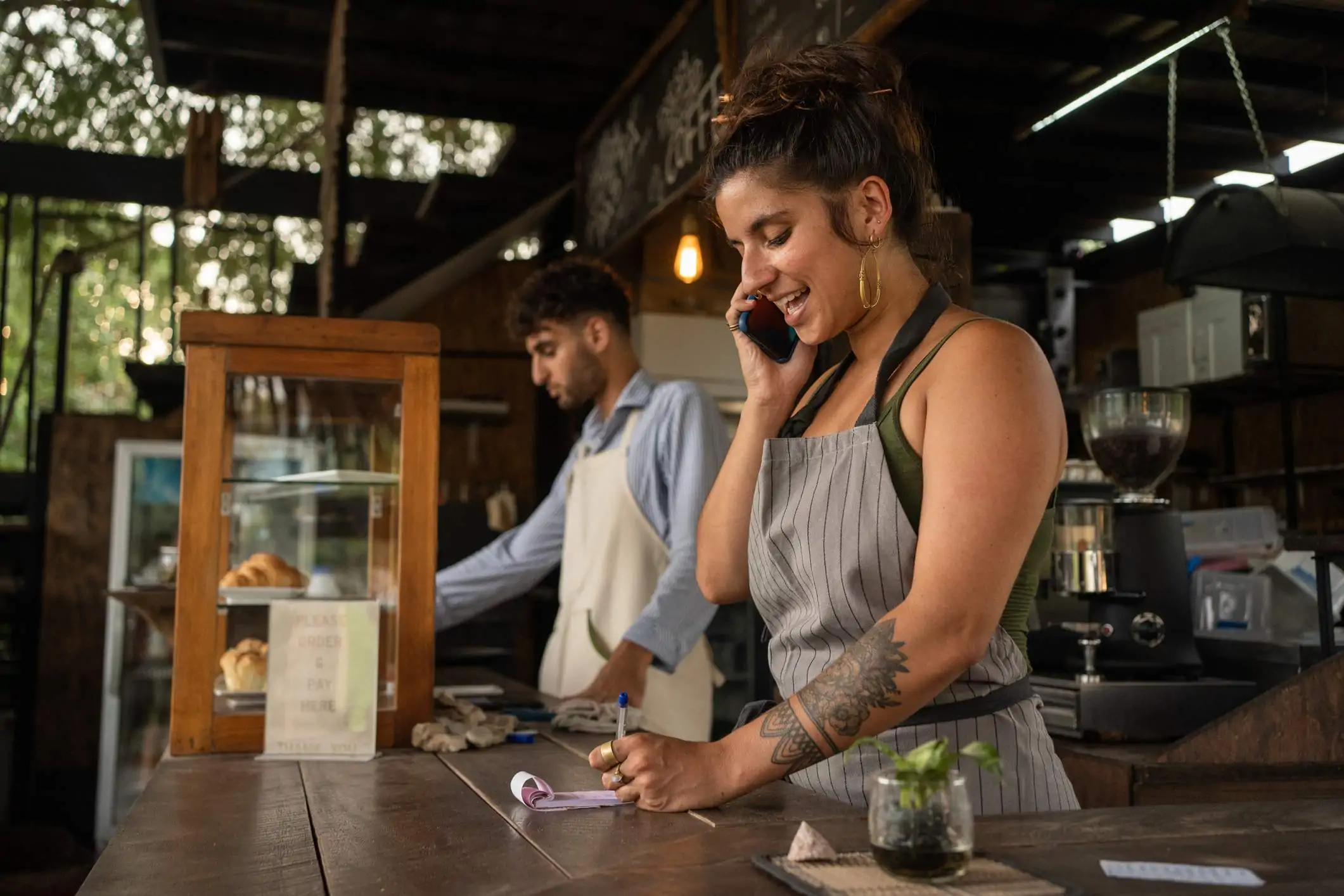 Image depicts a restaurant worker talking on the phone as they take an order on a pad of paper.