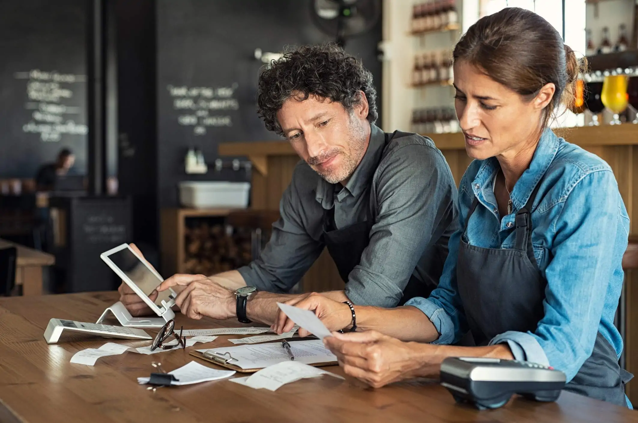 Image depicts two restaurant workers discussing finances.