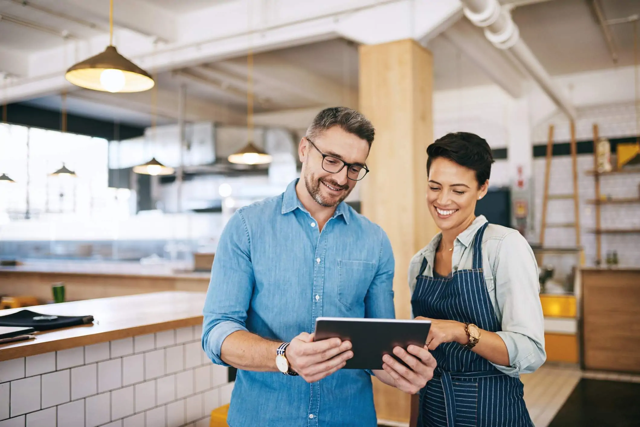 Image depicts two restaurant workers having a discussion over a tablet.