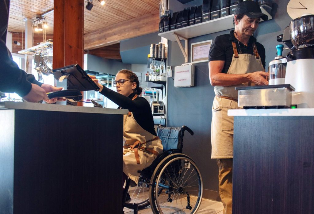 Restaurant cashier in wheelchair helps a guest settle their check