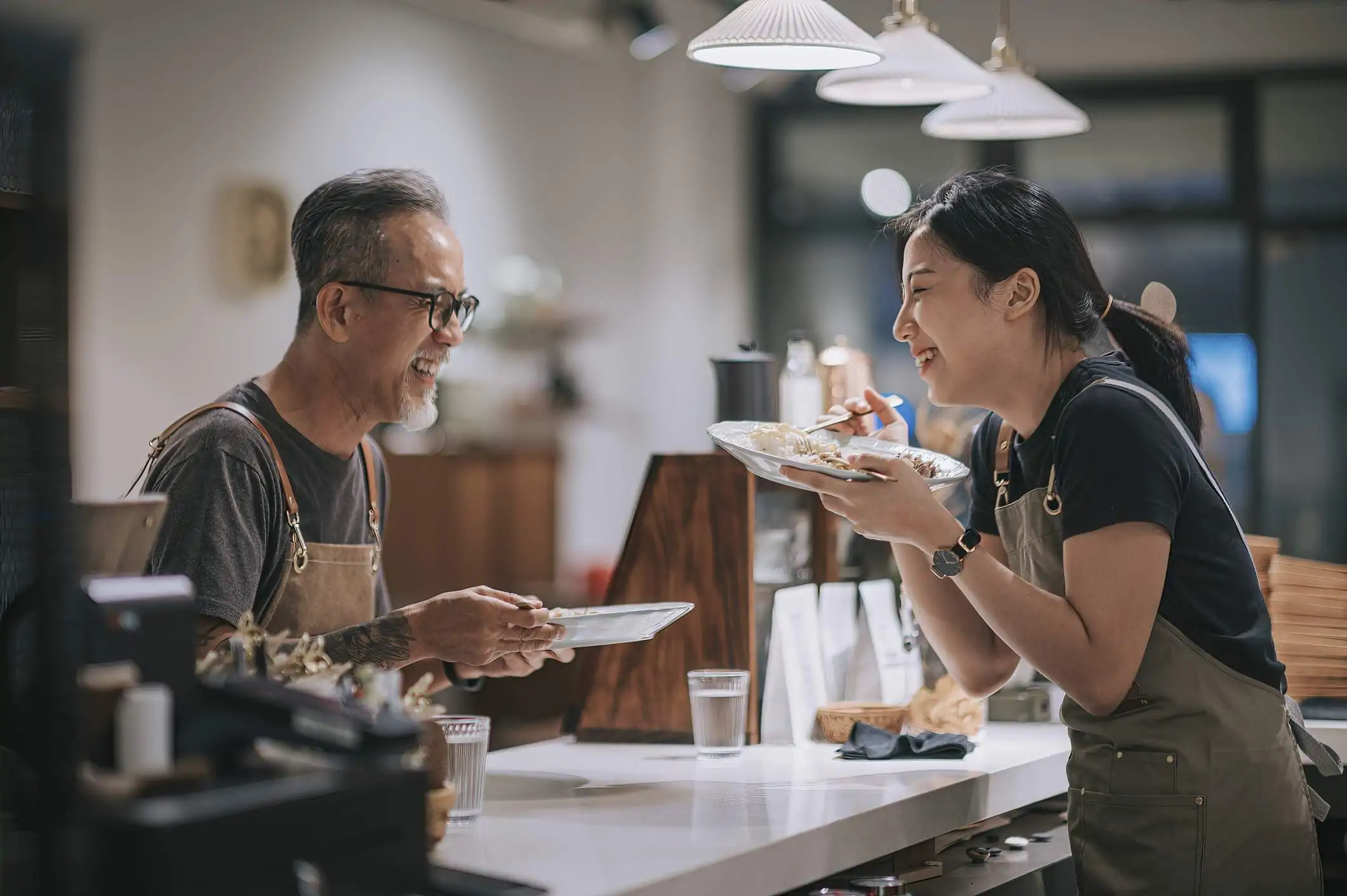 Image depicts two restaurant workers sharing a meal and laughing.