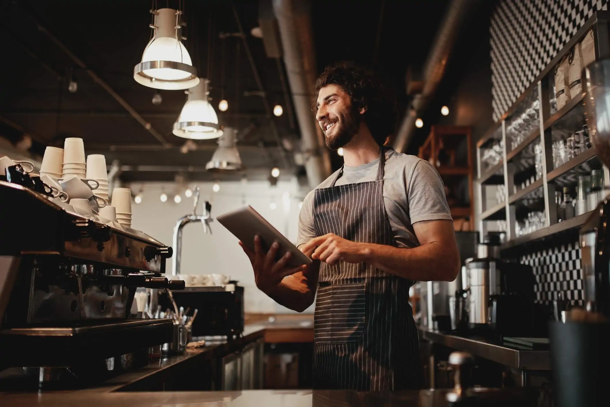 Image depicts a restaurant worker using a tablet and smiling.