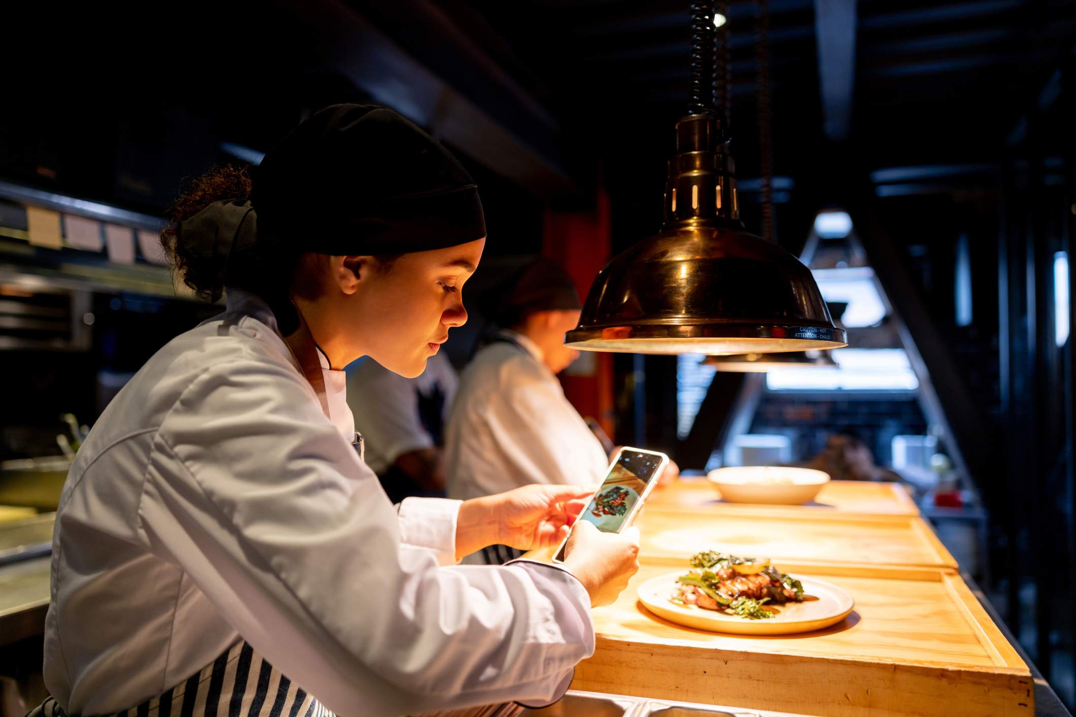 Image depicts a restaurant worker photographing food. 