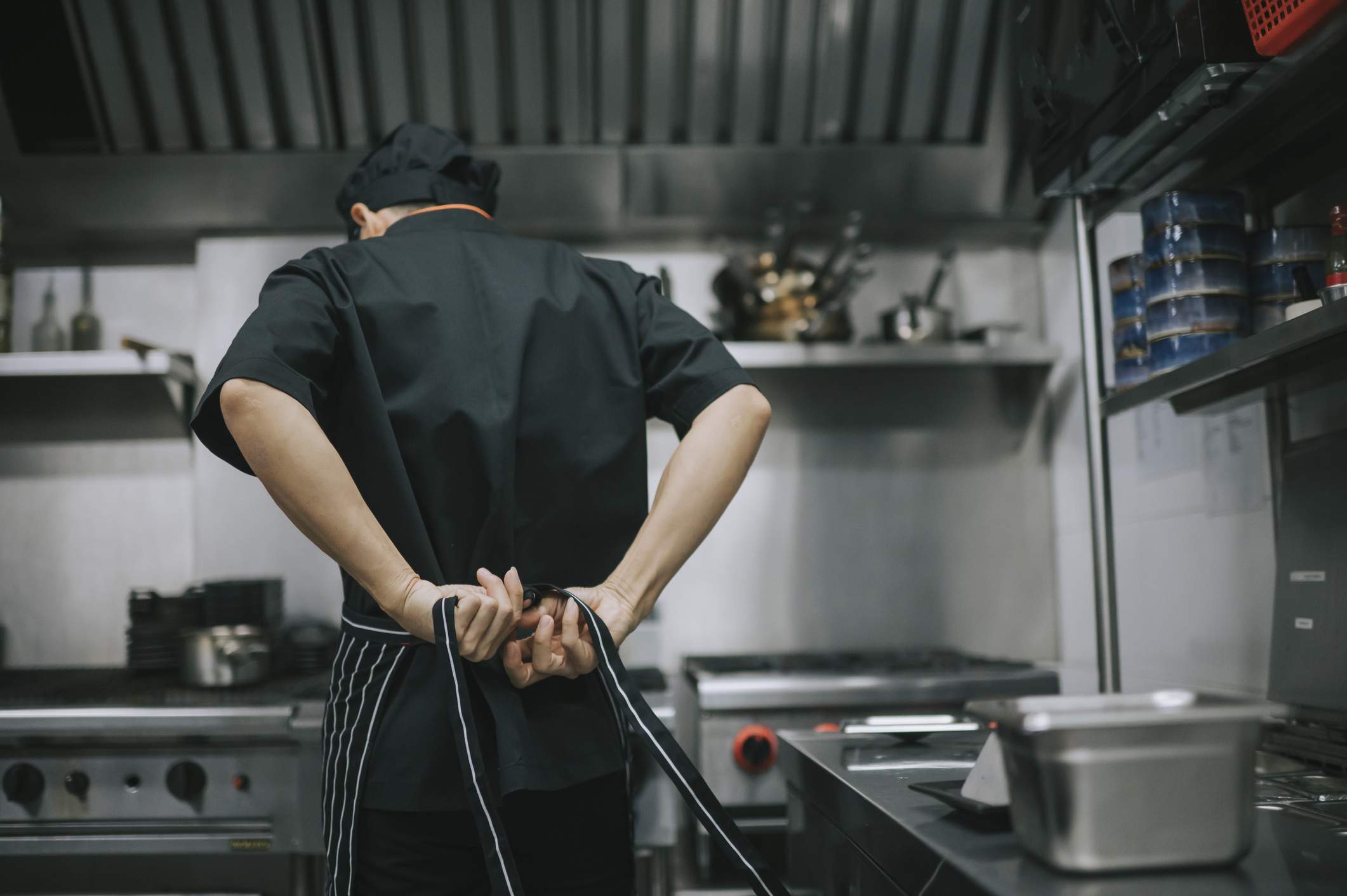 Image depicts a restaurant worker tying an apron behind their back. 