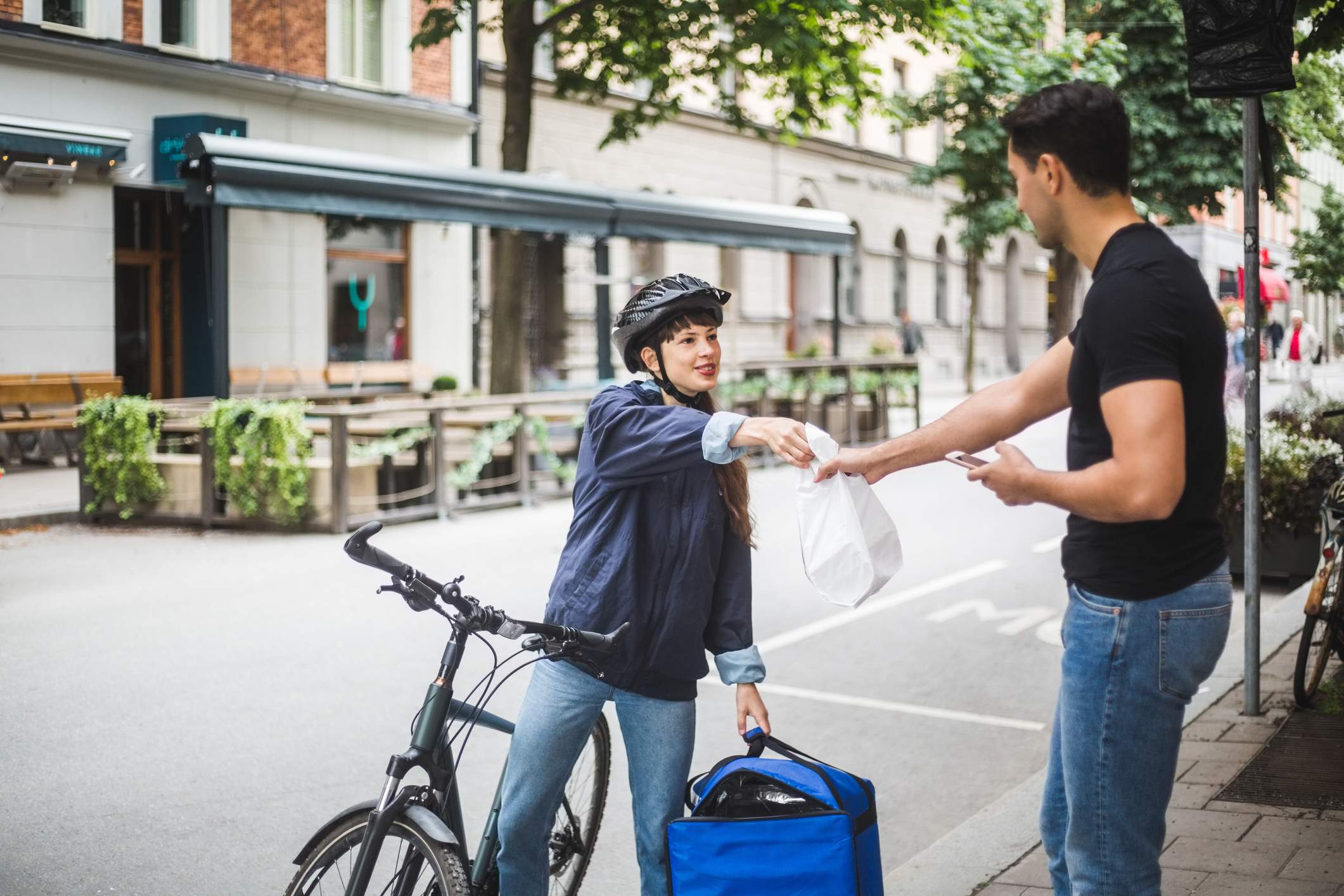 Image depicts a delivery driver handing off food to a customer. 