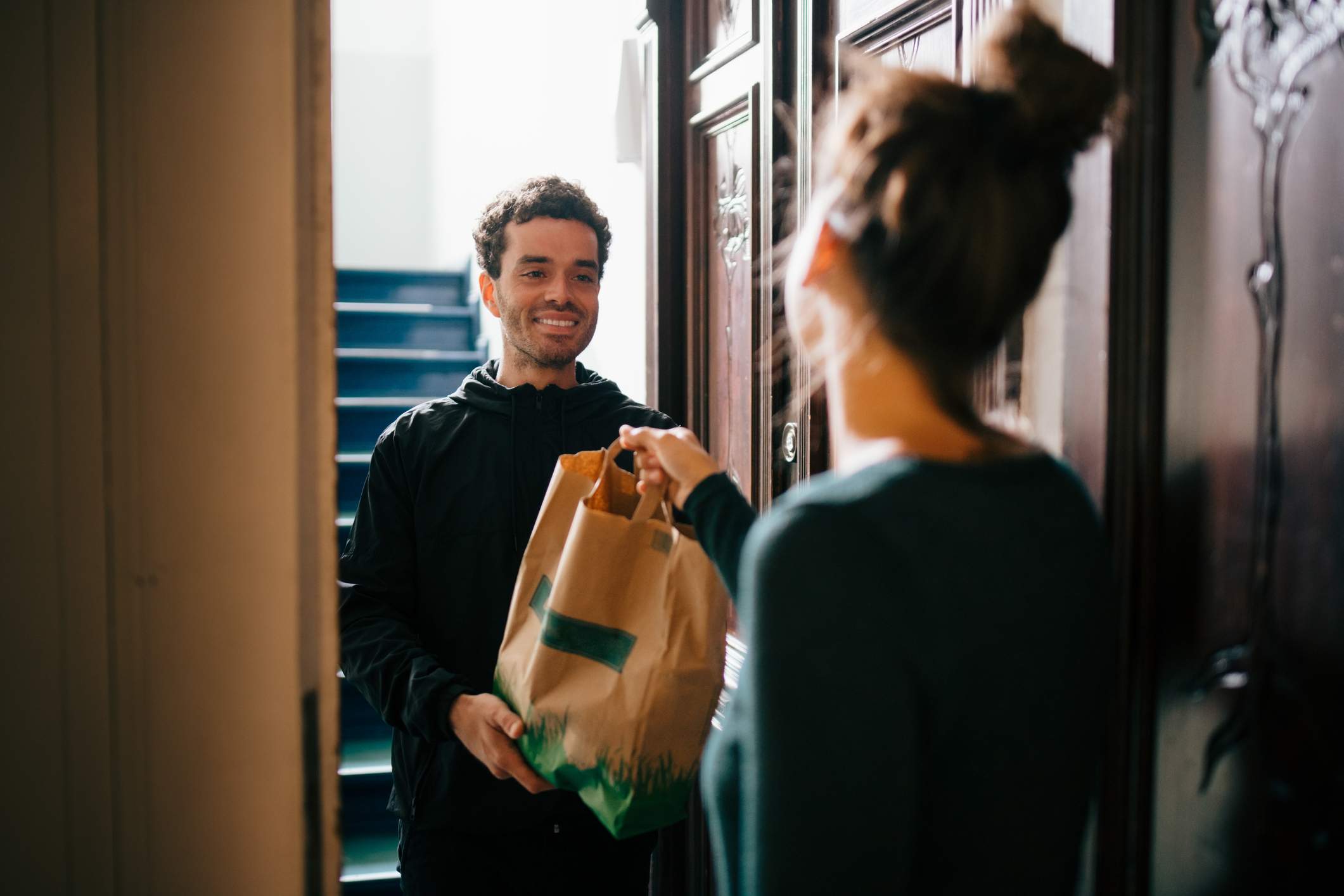 Image depicts a customer accepting food from a delivery driver.