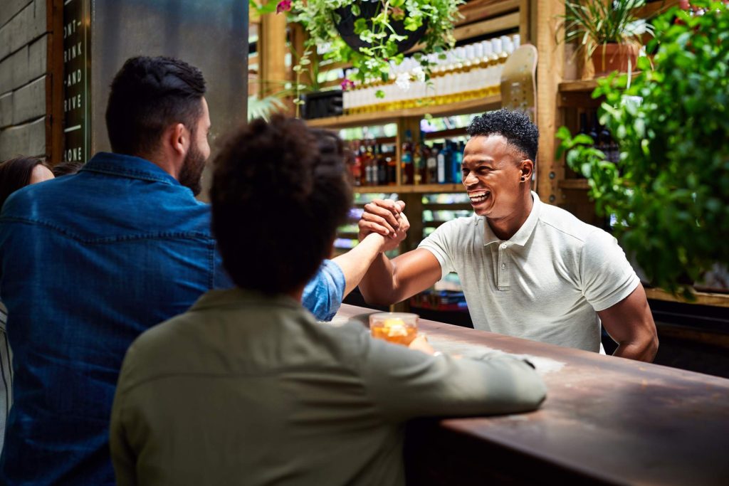 Image depicts two diners greeting a bartender. 