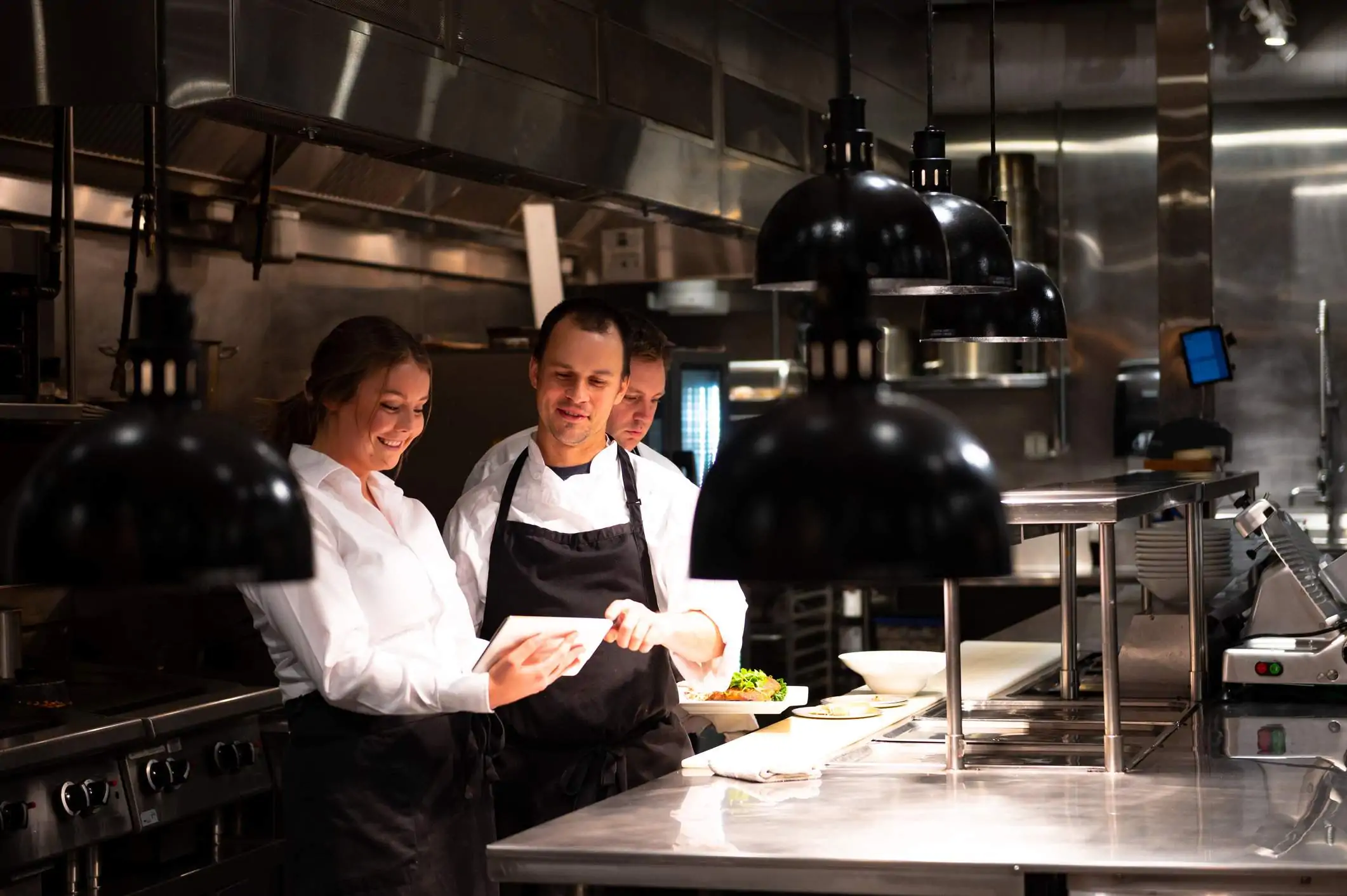 Image depicts three restaurant workers looking at a tablet.