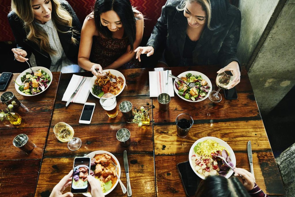 Image depicts a group of diners using phones at a restaurant table.